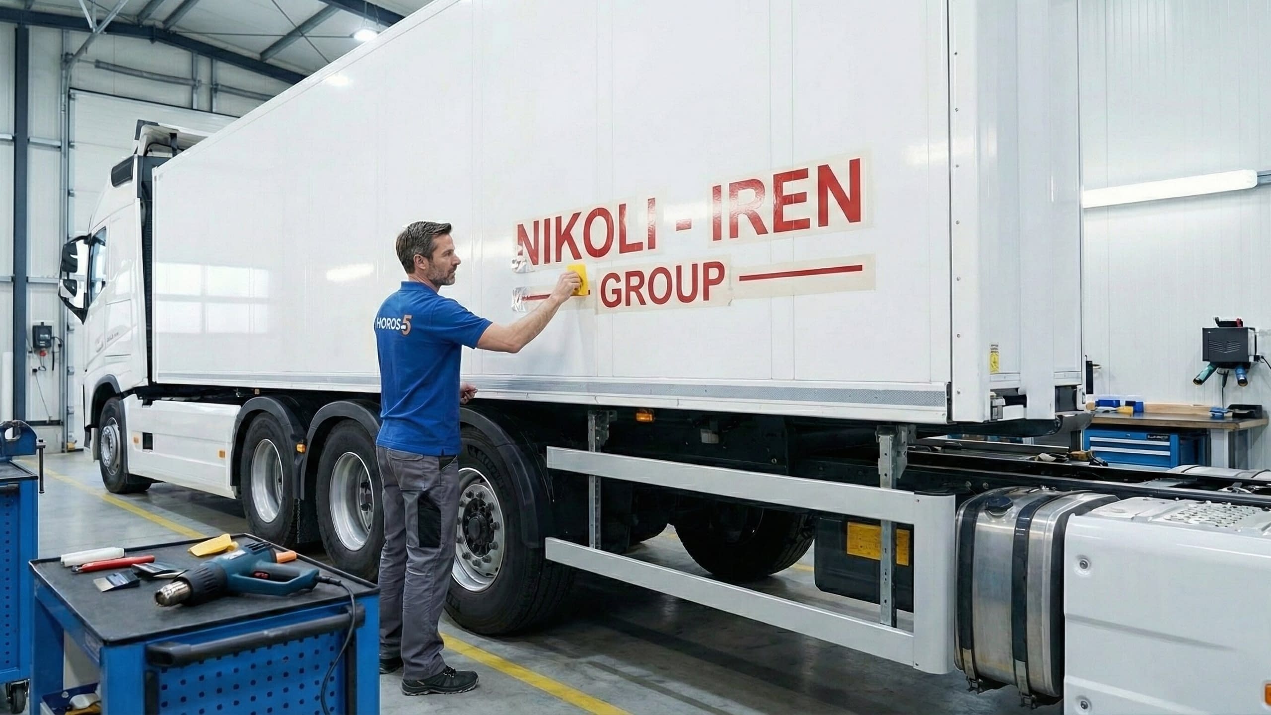 Професионален монтажист на Хорос 5 апликира плотерно изрязани рекламни надписи от фолио върху гладката повърхност на ремарке на камион.