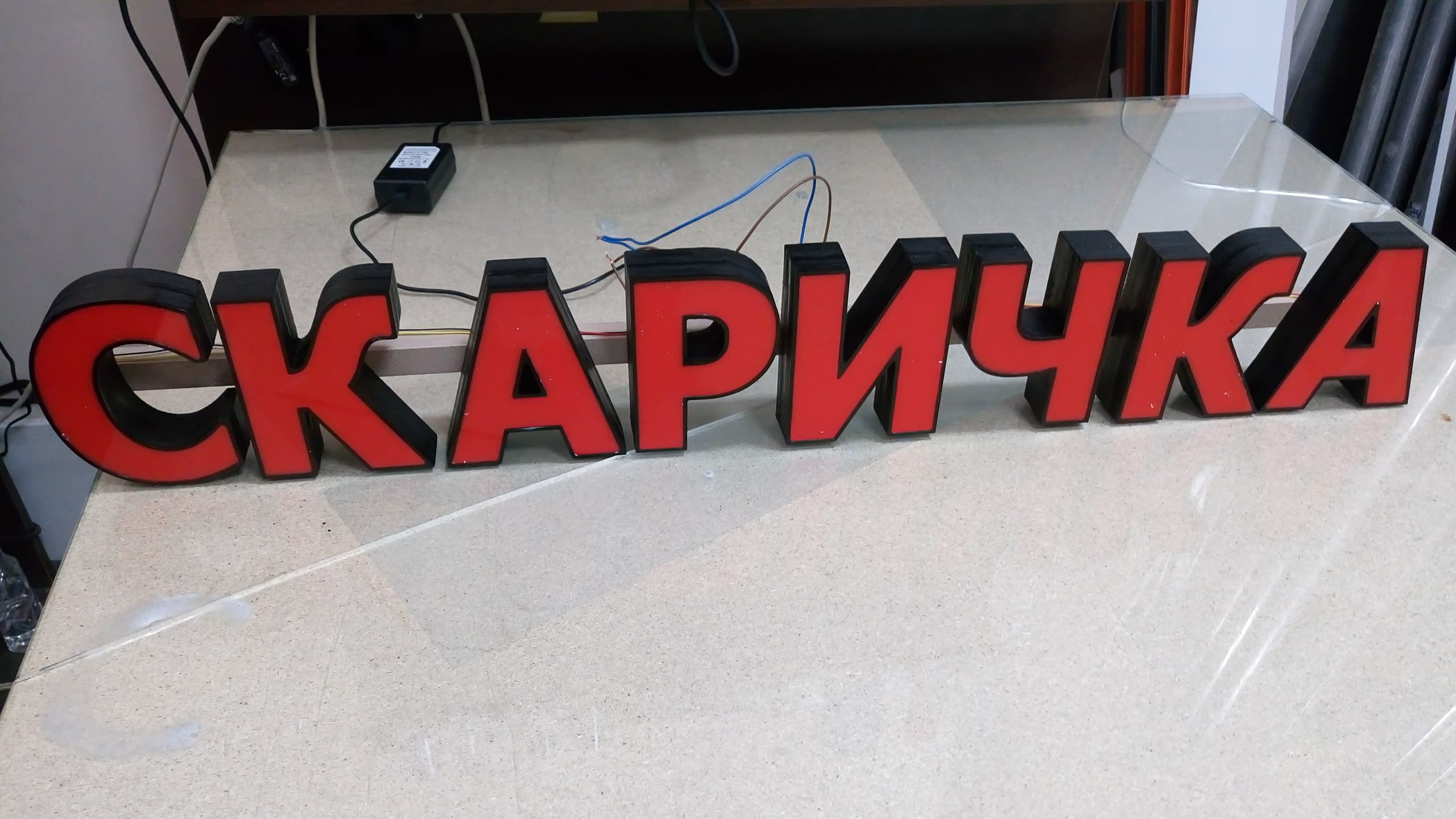 Готов за монтаж светещ надпис "СКАРИЧКА" от обемни букви с червено лице от плексиглас и черни страници.