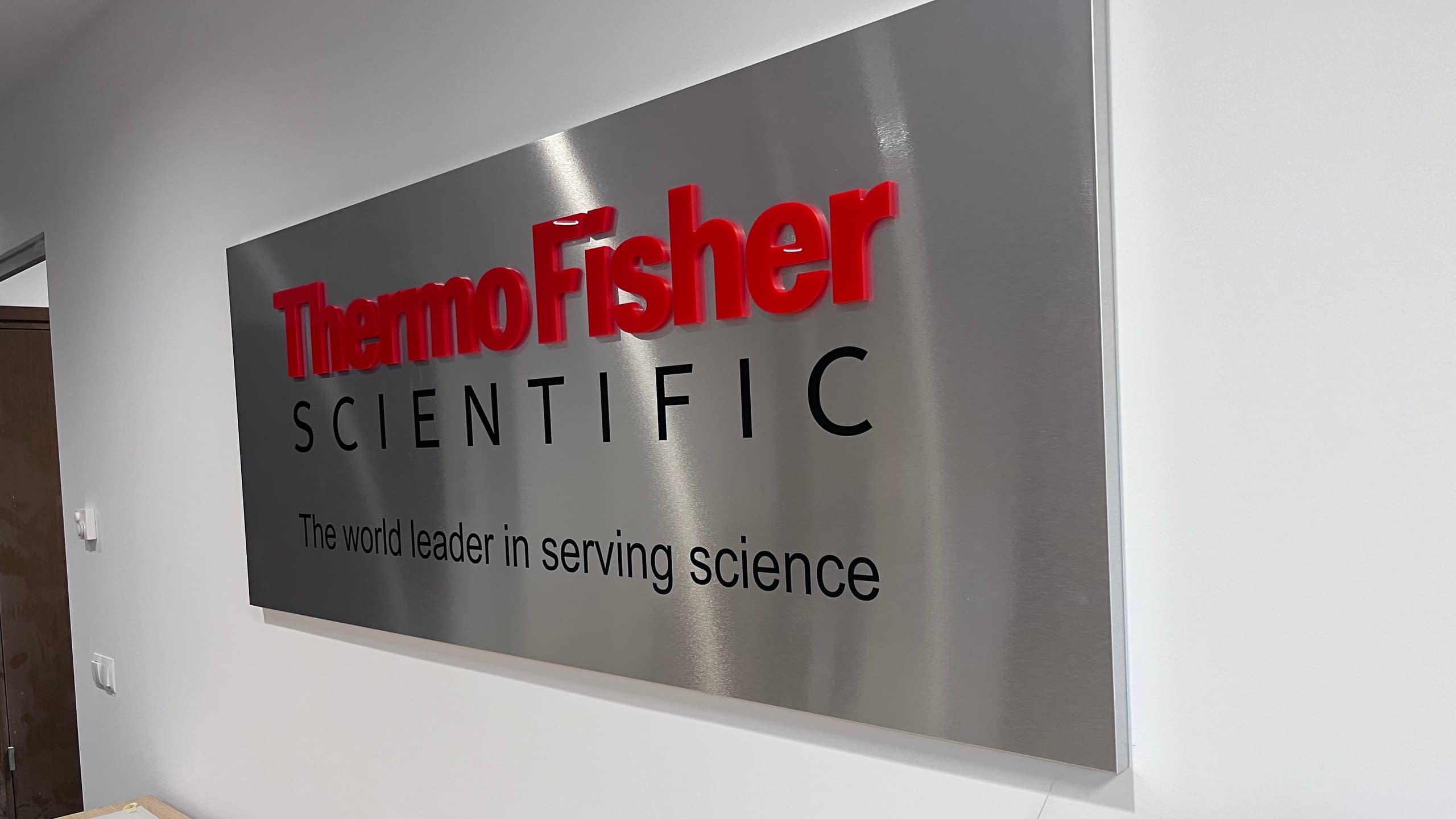 Голяма интериорна фирмена табела с основа от инокс и релефни обемни букви за компанията "Thermo Fisher SCIENTIFIC".