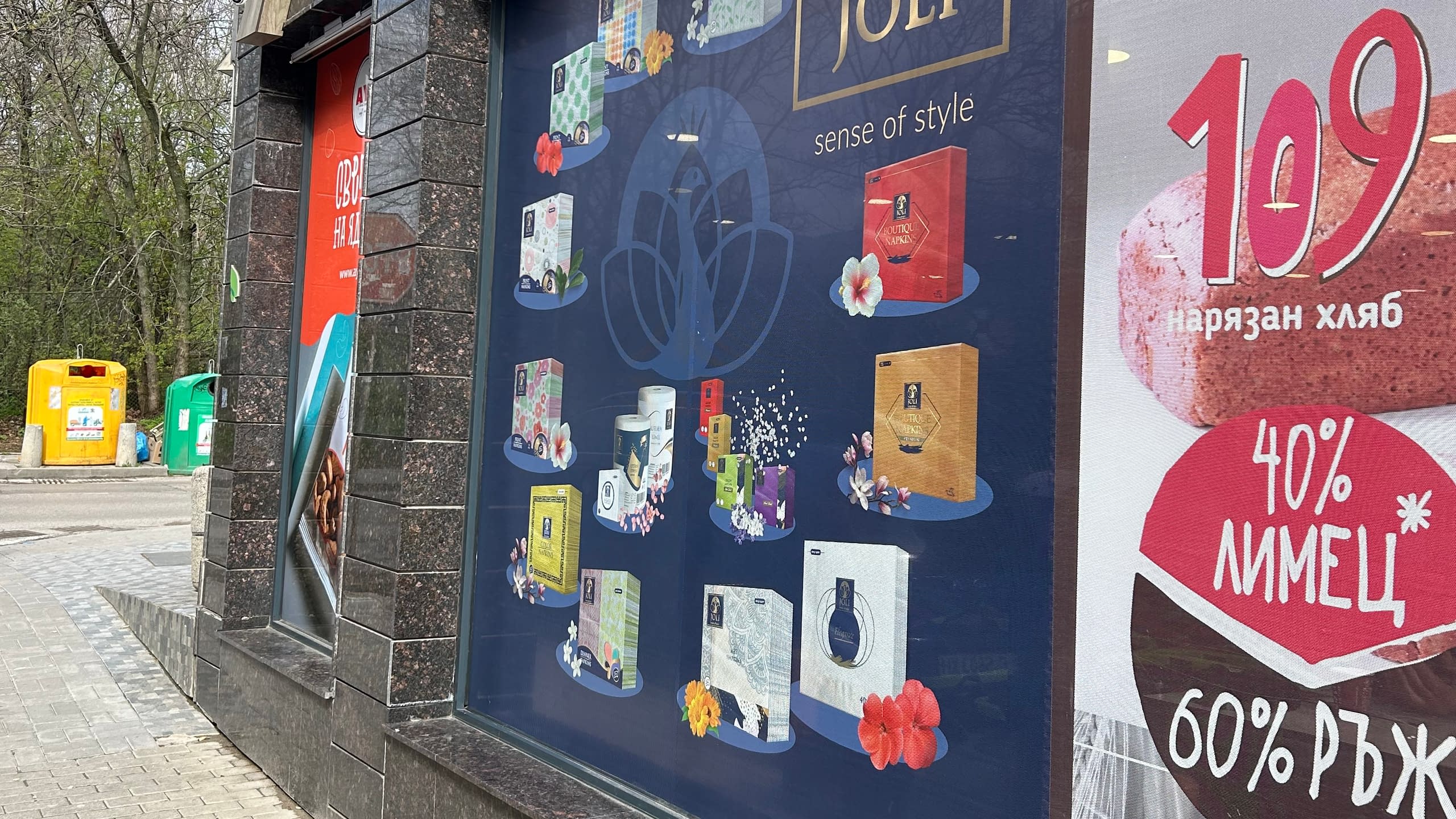 Витрини на магазин, фолирани с различни рекламни стикери с пълноцветен печат, показващи продукти и промоционални оферти.