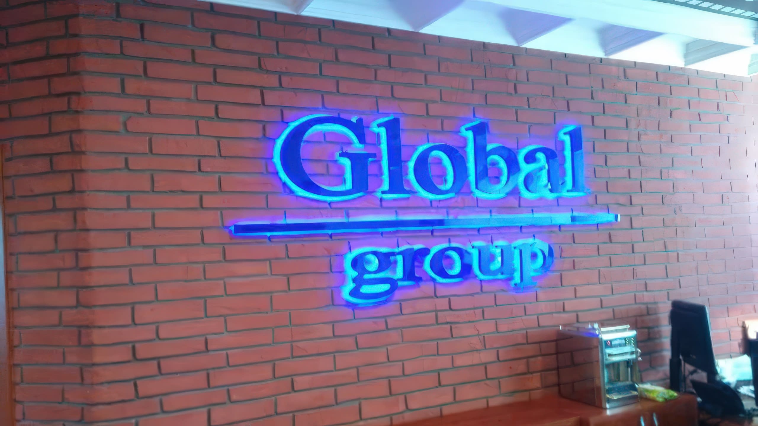 Светещи обемни букви в синьо "Global group", монтирани на тухлена стена в интериора на офис.