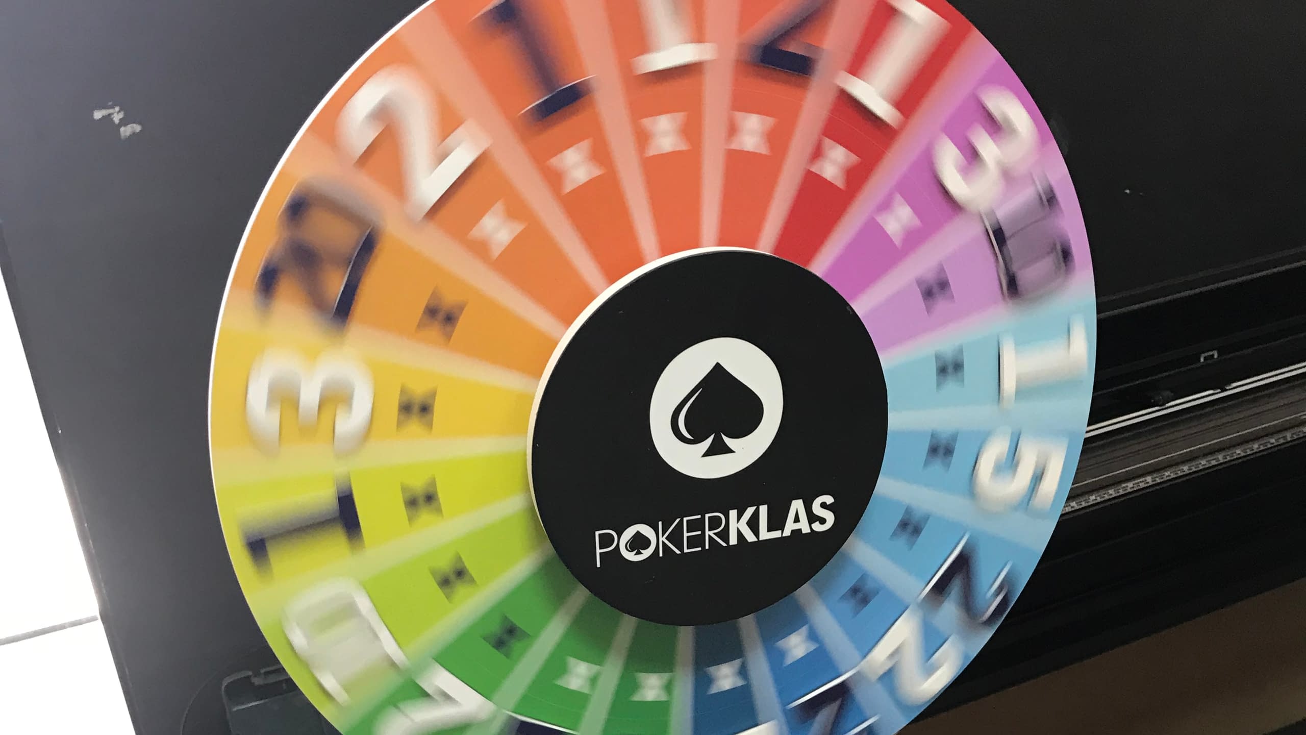 Колело на късмета в движение, показващо ефекта на завъртане. Брандирано е за POKERKLAS, с цветни сектори в цветовете на дъгата и числа.