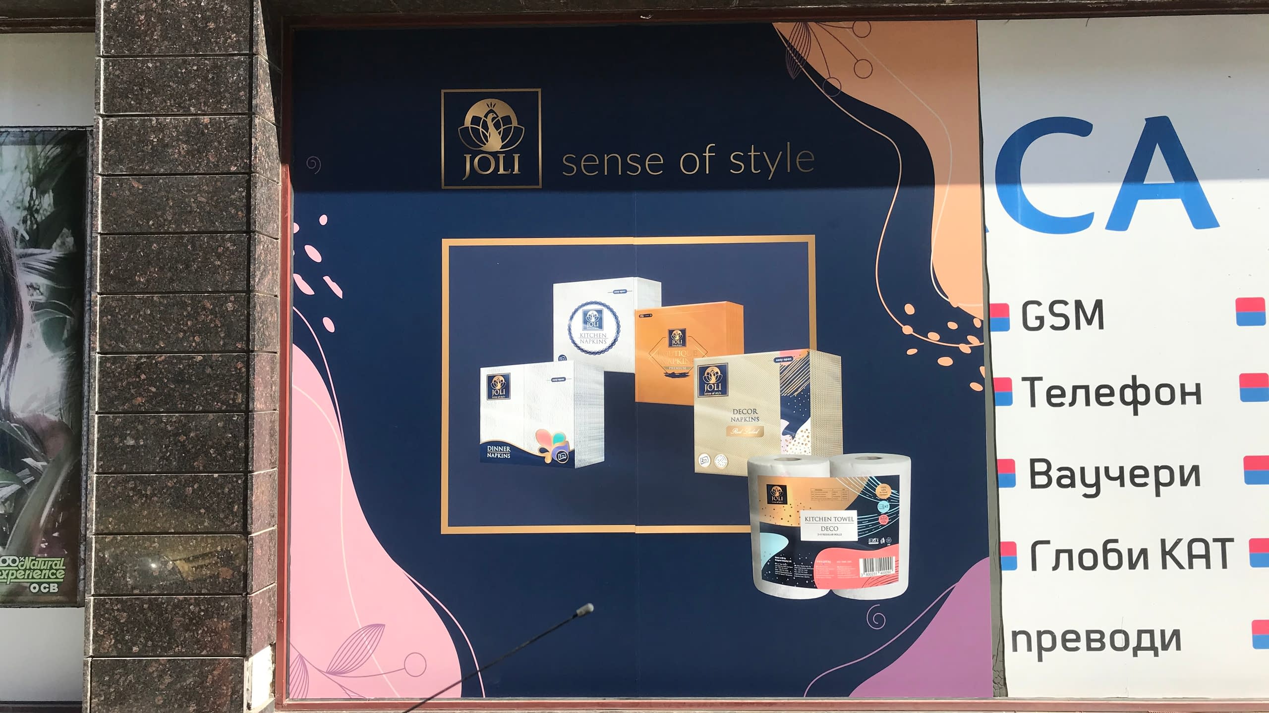 Рекламно фолио, залепено на витрина, показващо продуктова реклама на "JOLI sense of style" и списък с услуги.