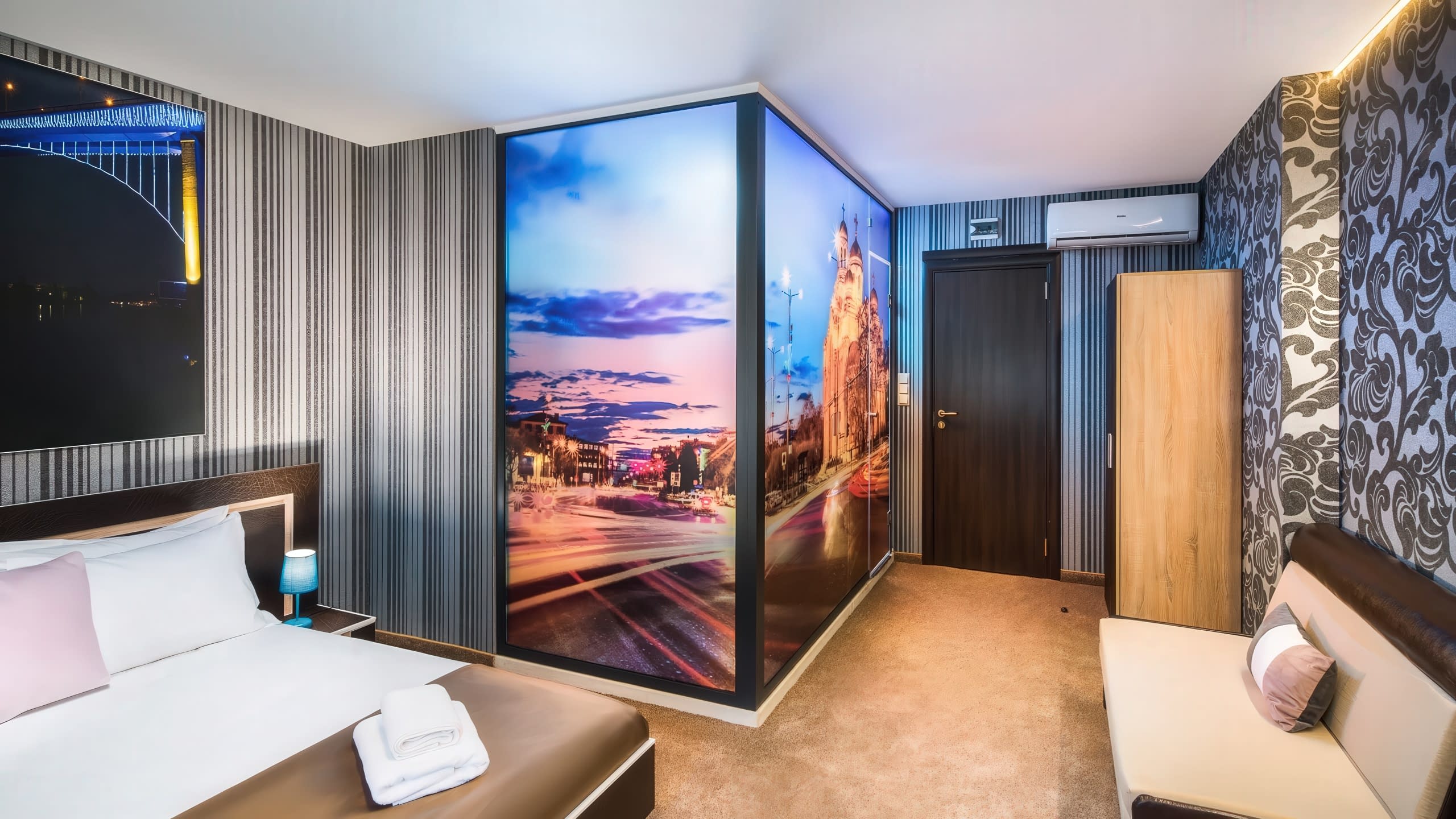Модерна хотелска стая с гардероб, изцяло облепен с декоративно фолио с пълноцветен печат на нощен градски пейзаж.