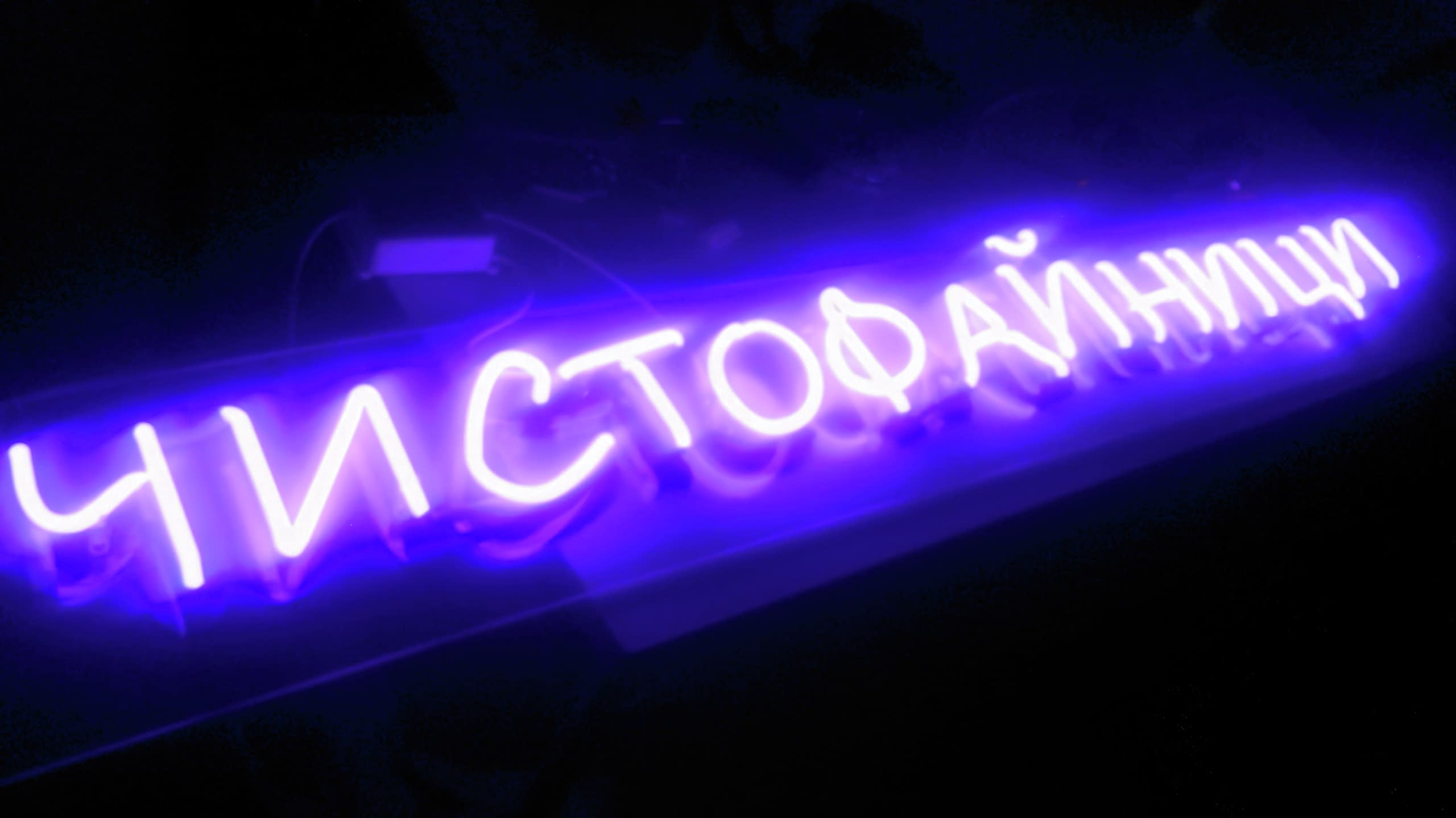 Ярък неонов надпис "Чистофайници", изписан ръкописно и светещ в наситено лилав цвят на черен фон.