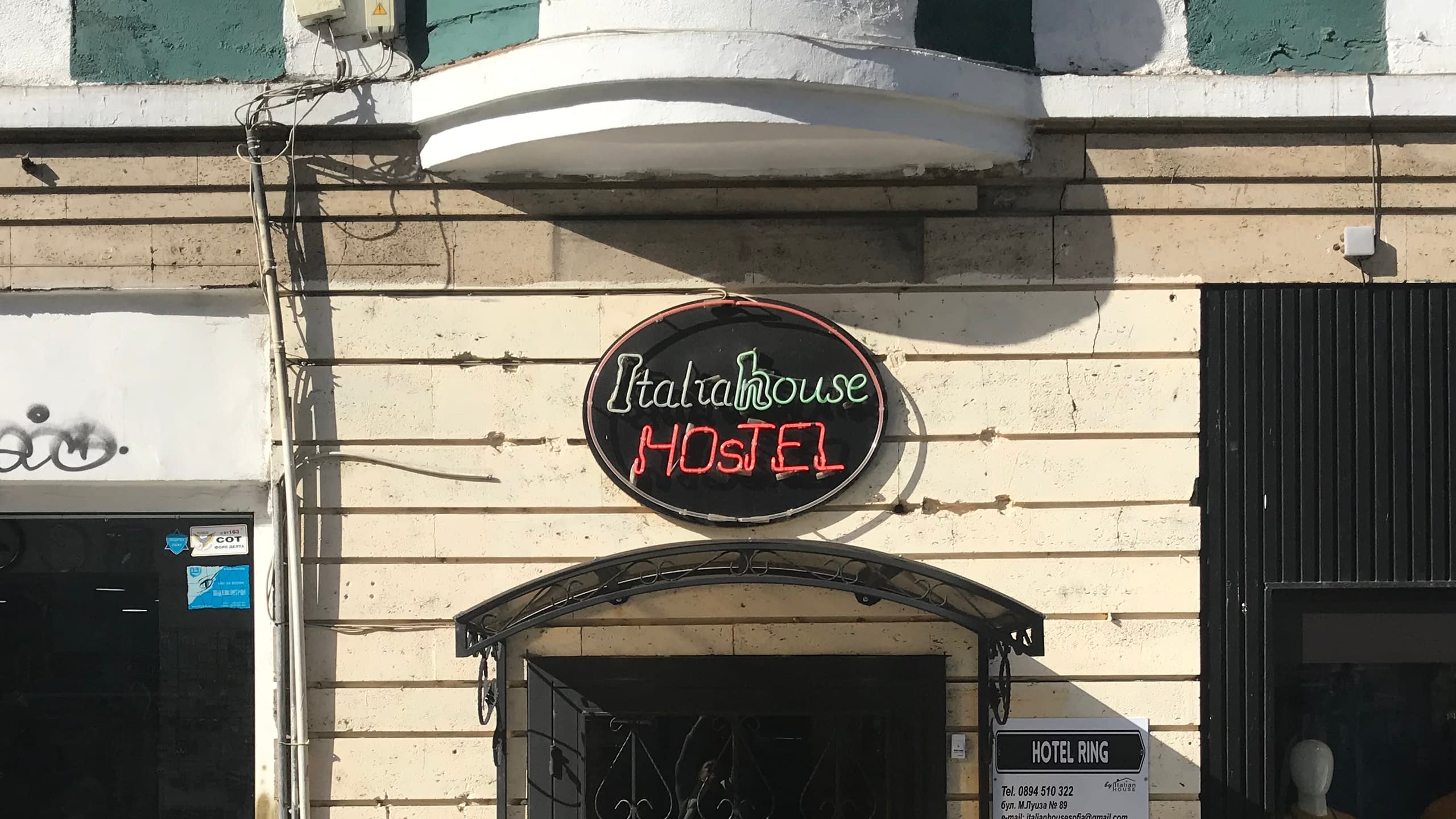 Ретро неонова табела на "Italiahouse HOSTEL" със зелен и червен неон, монтирана на фасада на сграда.