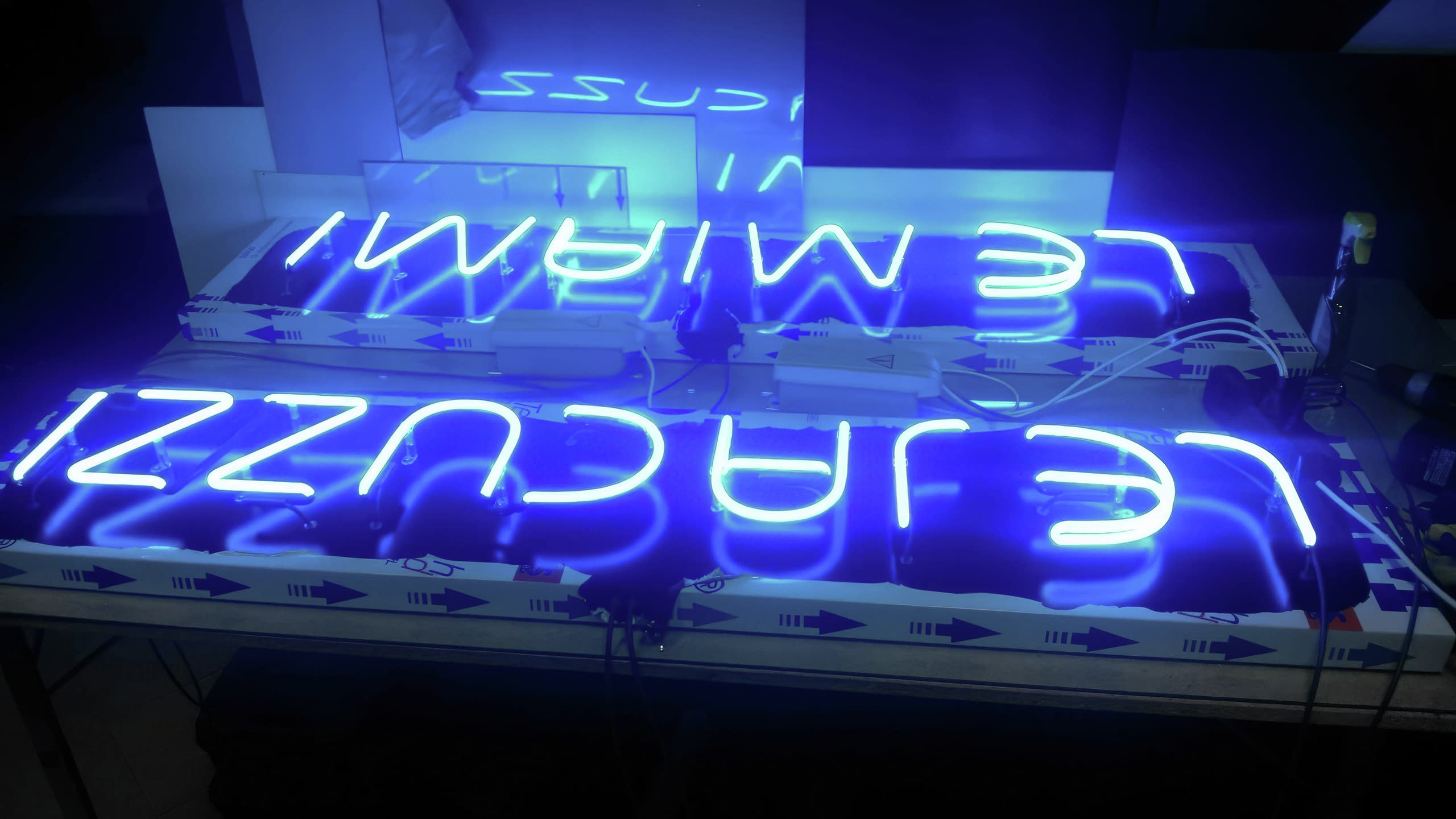 Две готови неонови реклами - "Le Miami" и "Le Jacuzzi", светещи в яркосиньо по време на тест в работилница.