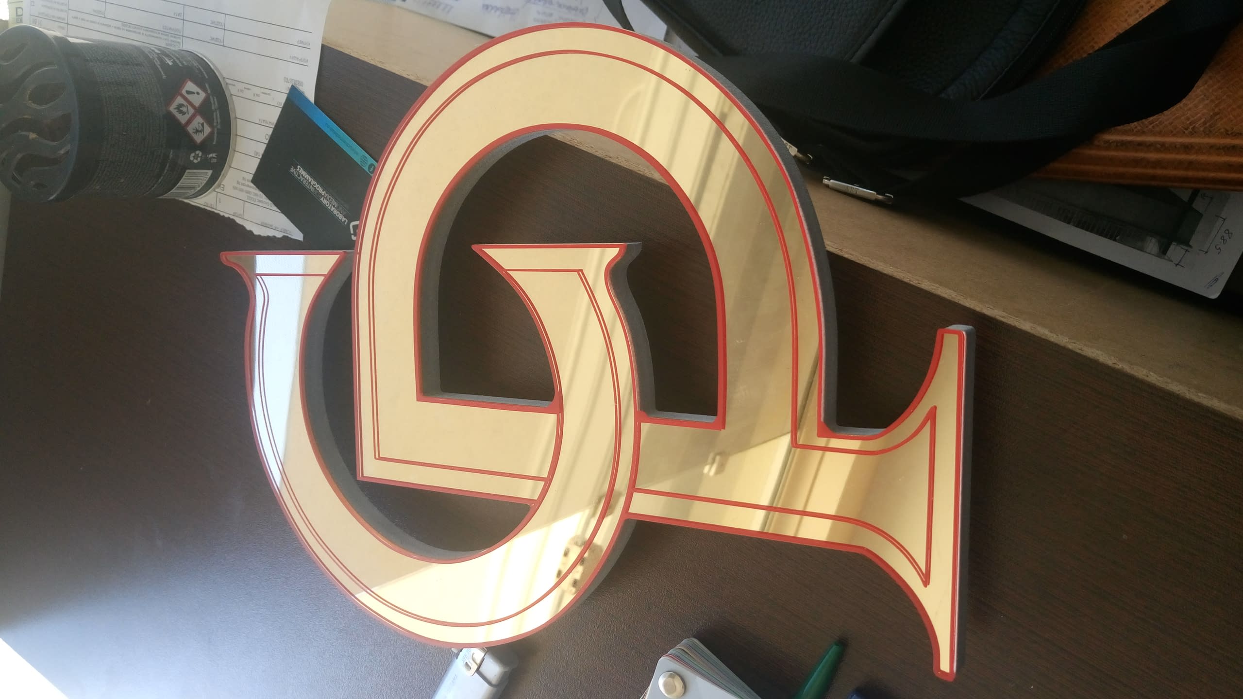 Декоративно обемно лого от огледален златен плексиглас с червени кантове, предназначено за интериорна украса.