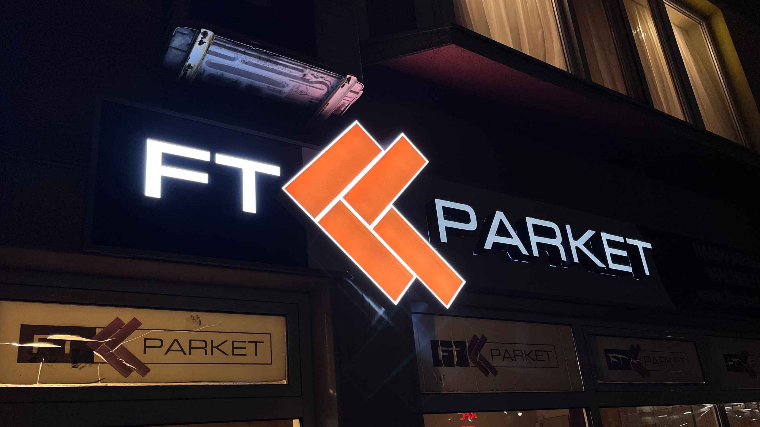 Светеща рекламна табела на магазин "FT Parket" през нощта, с обемни букви от плексиглас и ярко оранжево лого.