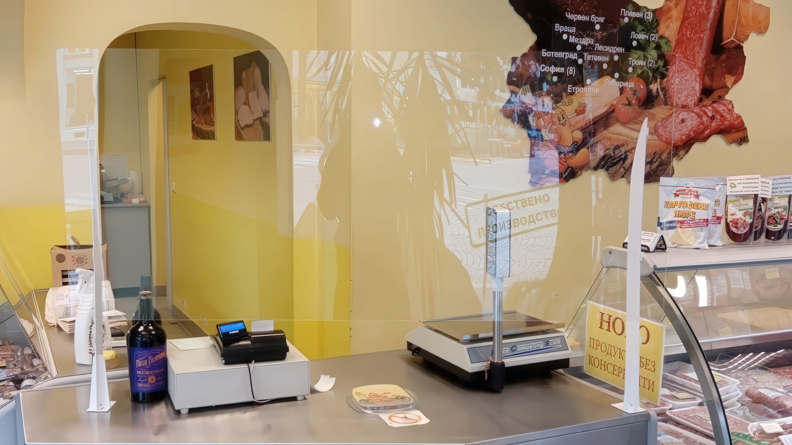 Предпазен параван от плексиглас, поставен на щанд в хранителен магазин пред касов апарат и везна.