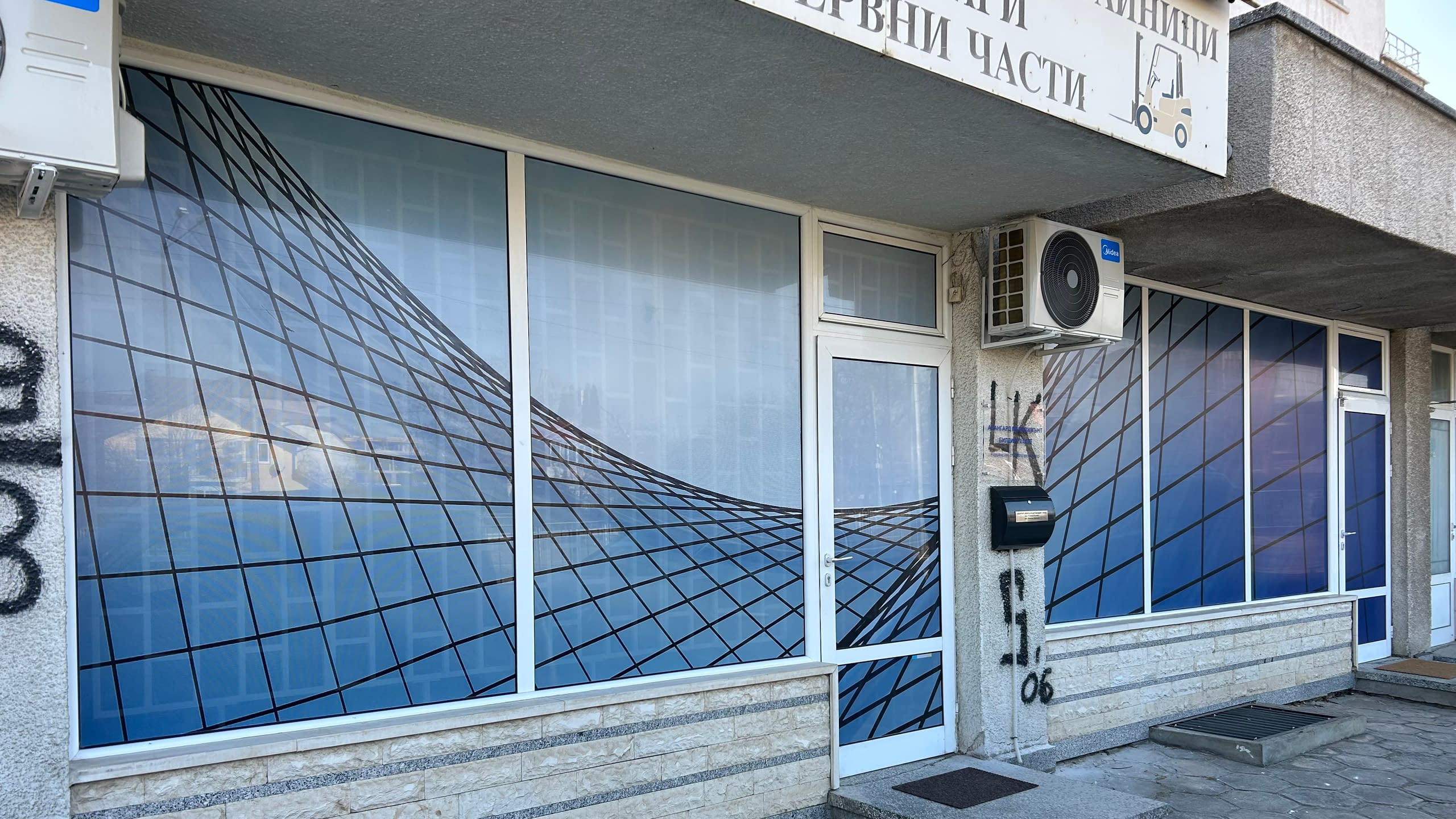 Фасада на магазин с витрини, изцяло облепени с перфо фолио със синя абстрактна графика.