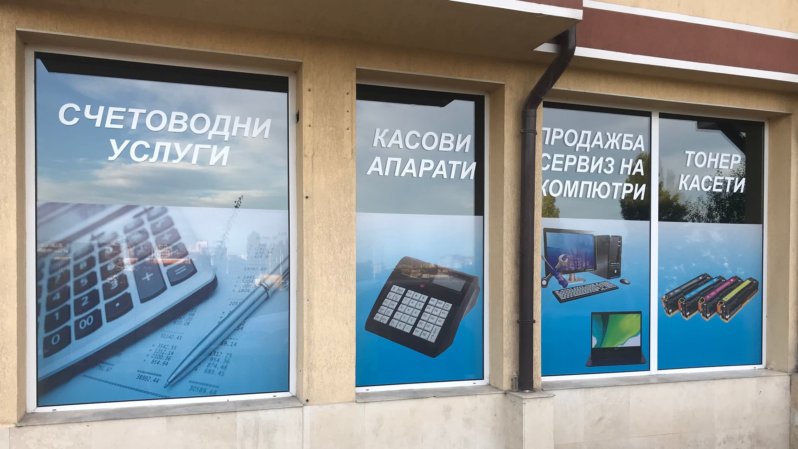 Три прозореца на офис, облепени с перфо фолио, рекламиращи счетоводни услуги, касови апарати и компютърен сервиз.