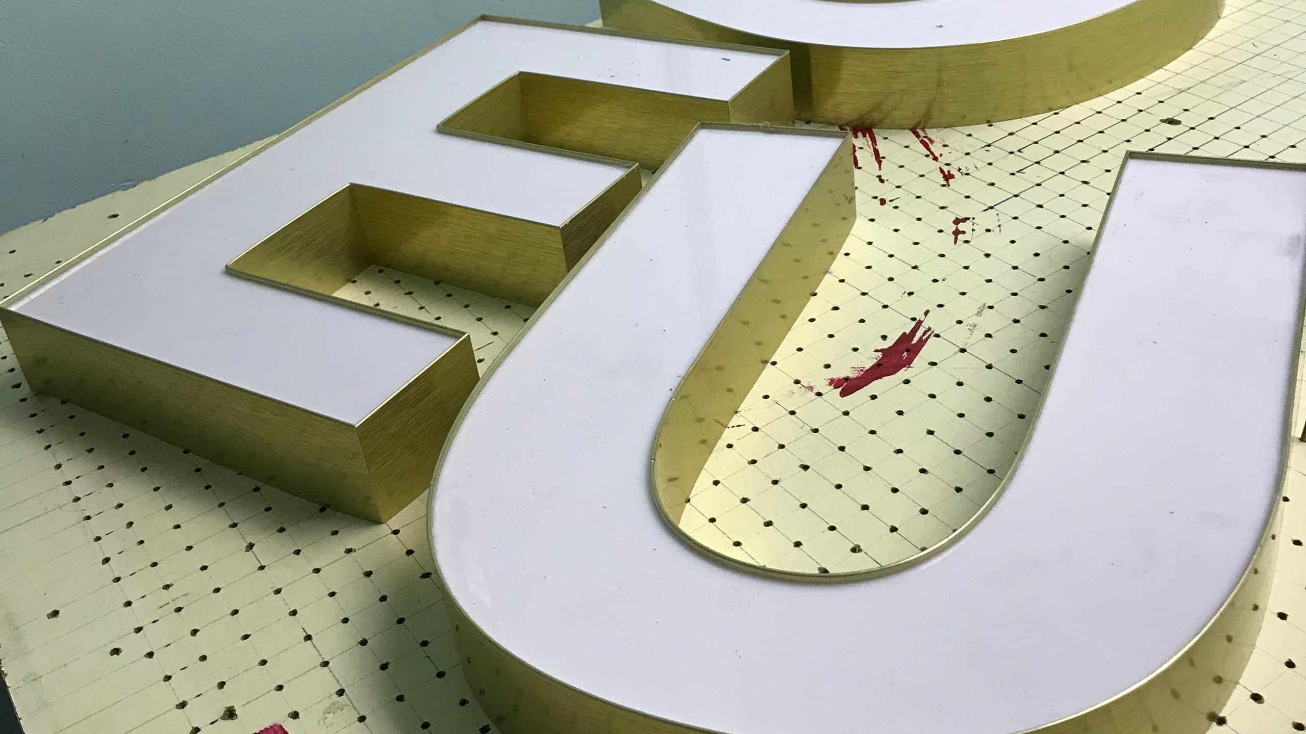 Близък план на големи обемни букви "EU" със златни страници и бяло светещо лице от плексиглас, в процес на изработка.