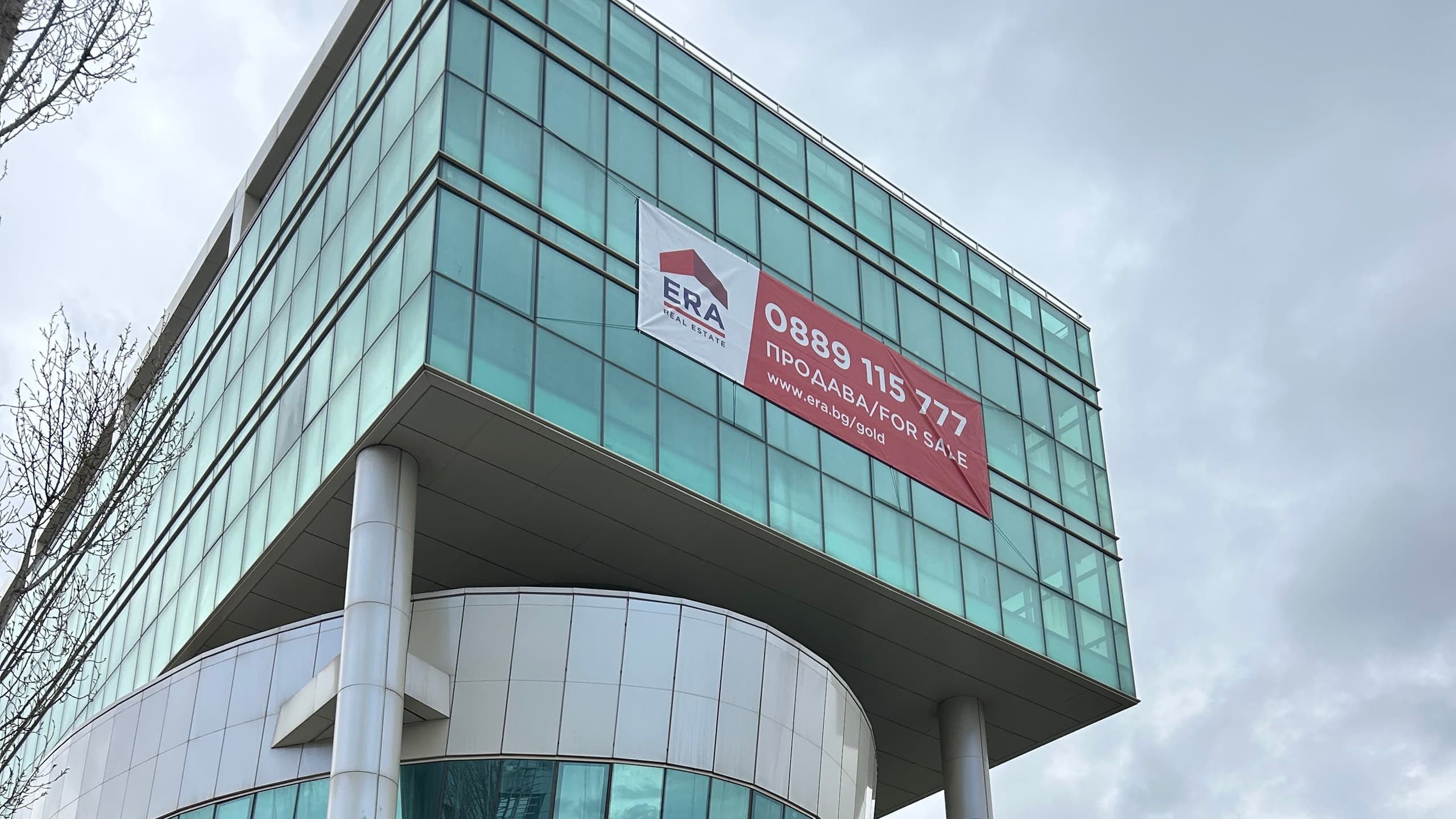 Голям рекламен винил на агенция за недвижими имоти "ERA", монтиран на стъклената фасада на модерна офис сграда.