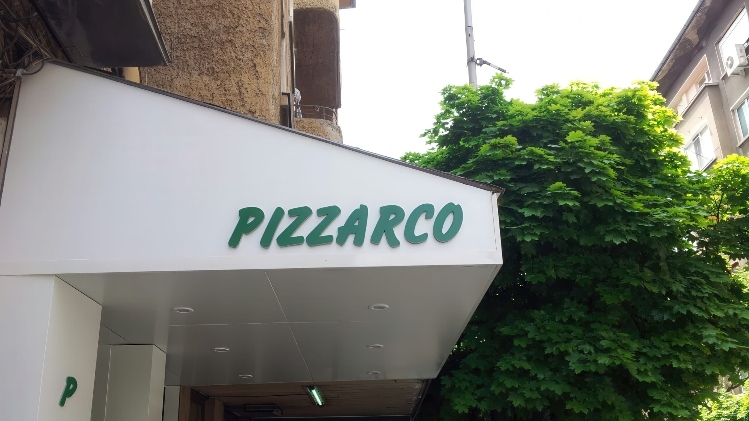 Табела с несветещи обемни букви в зелен цвят с надпис "PIZZARCO", монтирана върху бяла козирка на заведение.