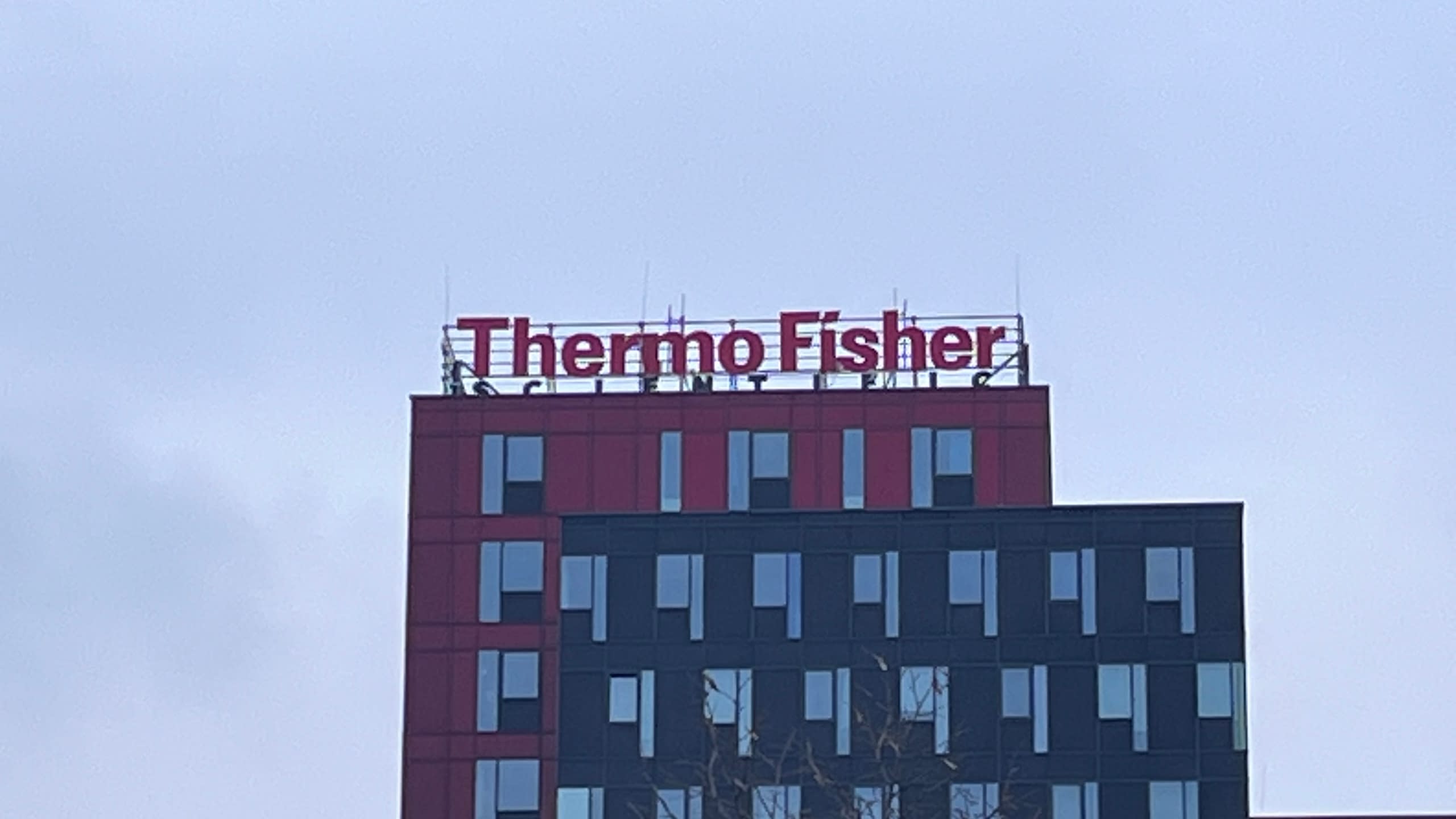 Покривна реклама с червени обемни букви на фирма "Thermo Fisher", монтирана на покрива на модерна бизнес сграда.
