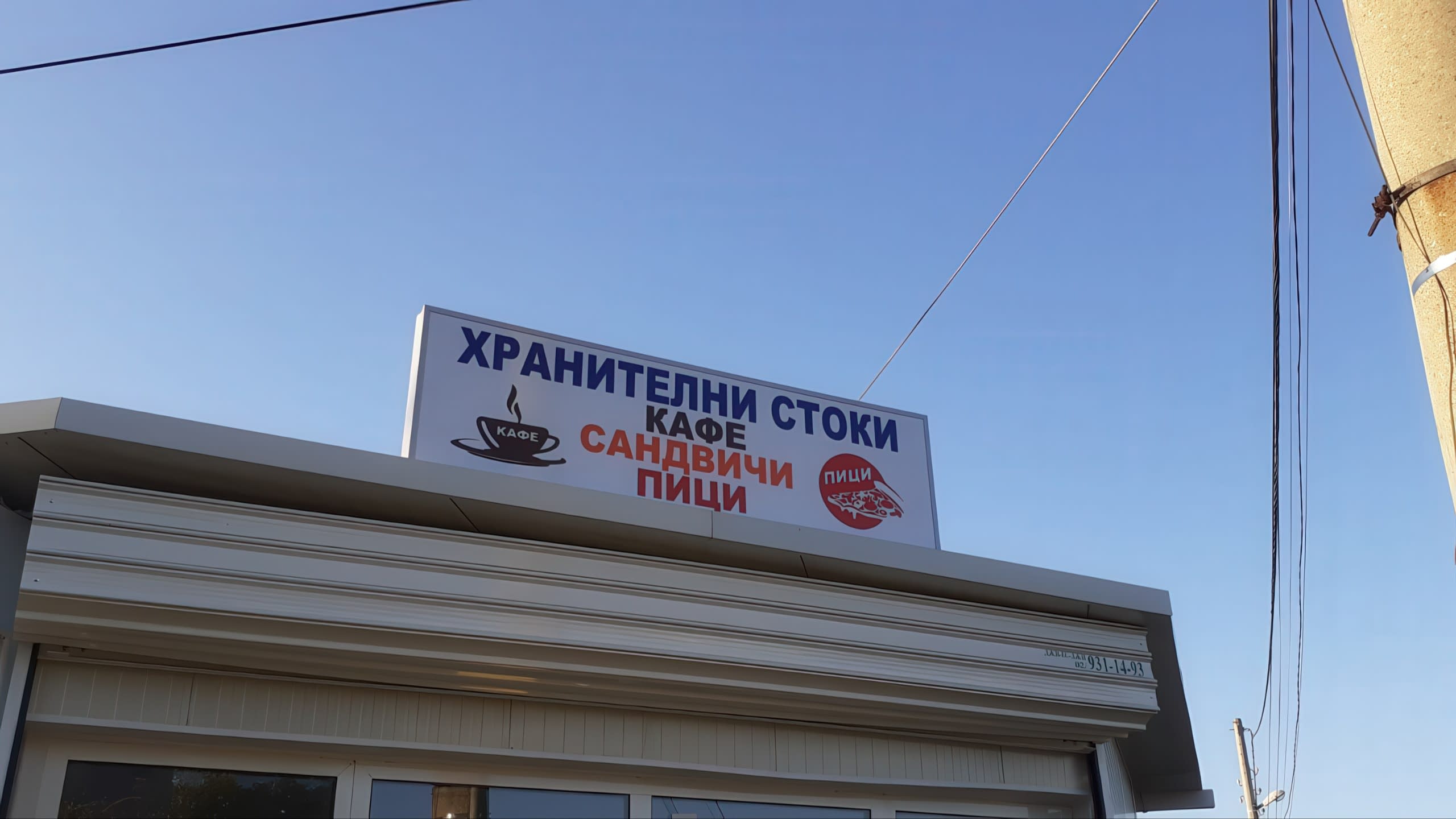 Светеща рекламна кутия на покрива на павилион с надписи "Хранителни стоки, Кафе, Сандвичи, Пици".
