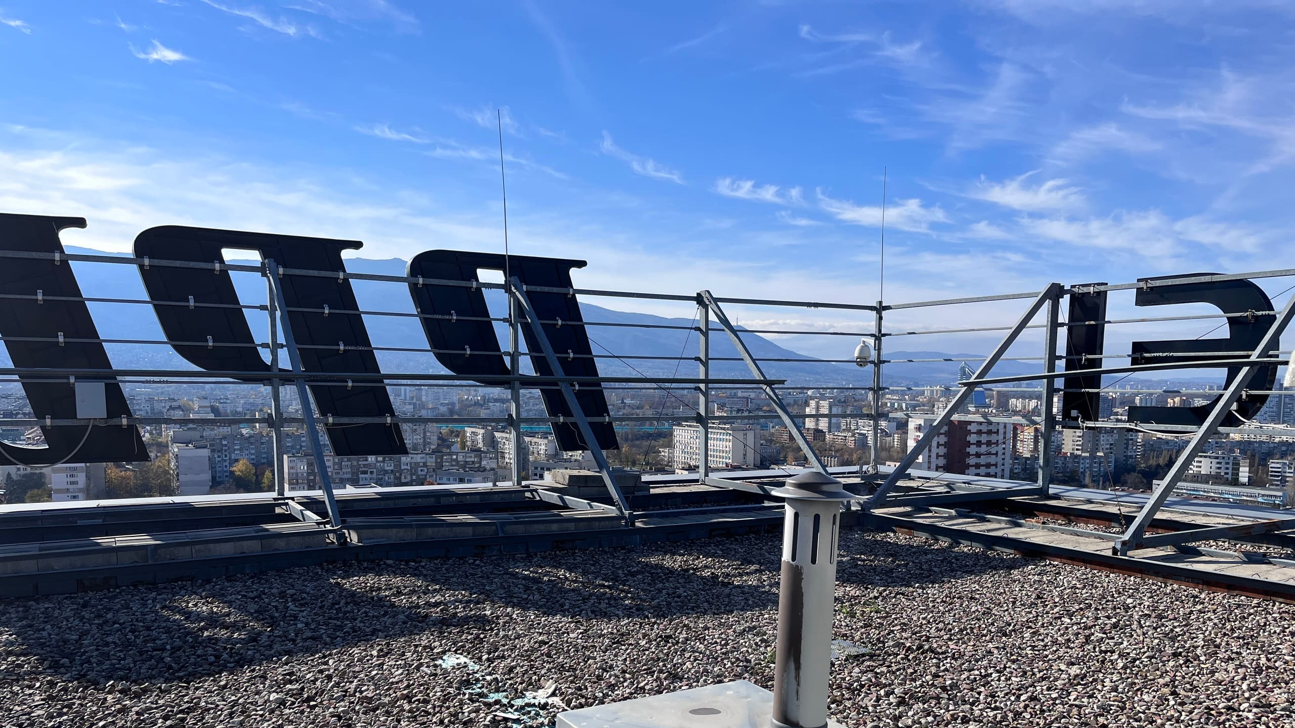 Гледка от покрив, показваща гърба на обемни букви и металната конструкция за монтаж на покривна реклама, на фона на панорамен изглед към София.