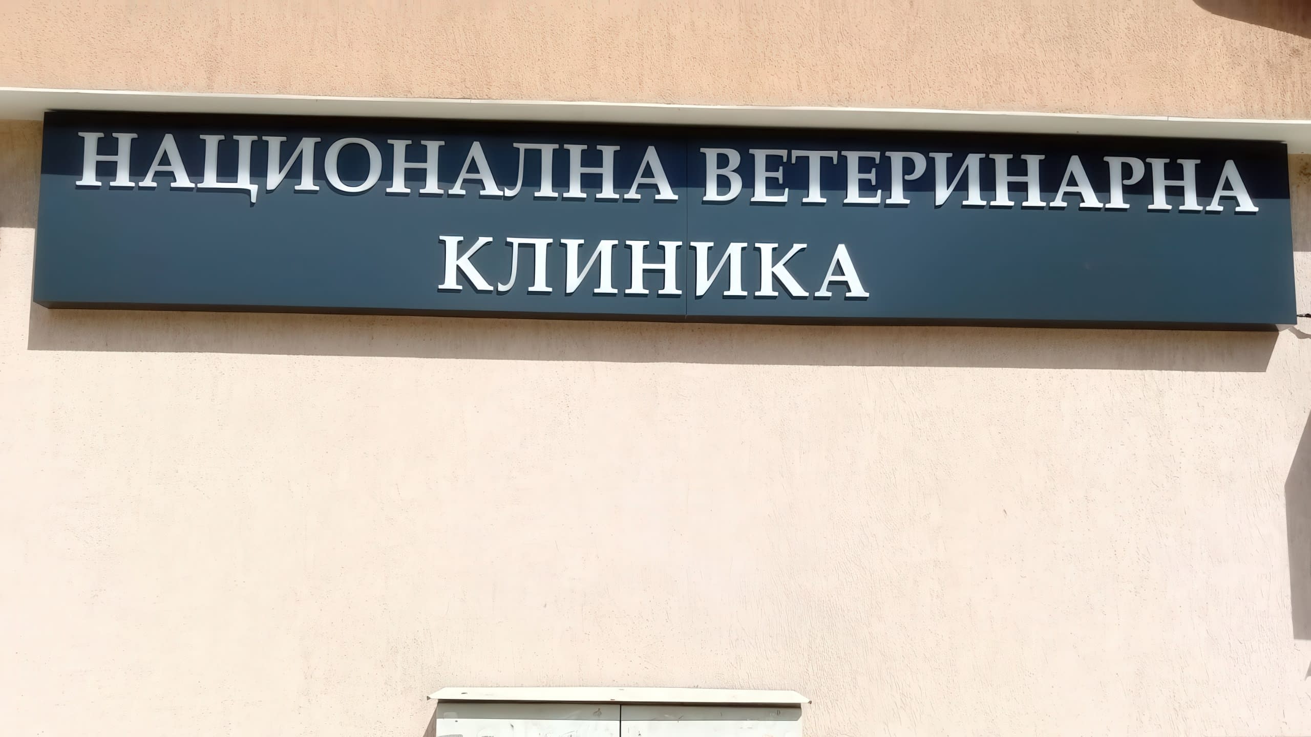 Монтирана несветеща рекламна табела на "Национална ветеринарна клиника". Стилна табела с бели обемни букви върху тъмна основа, поставена на фасада.