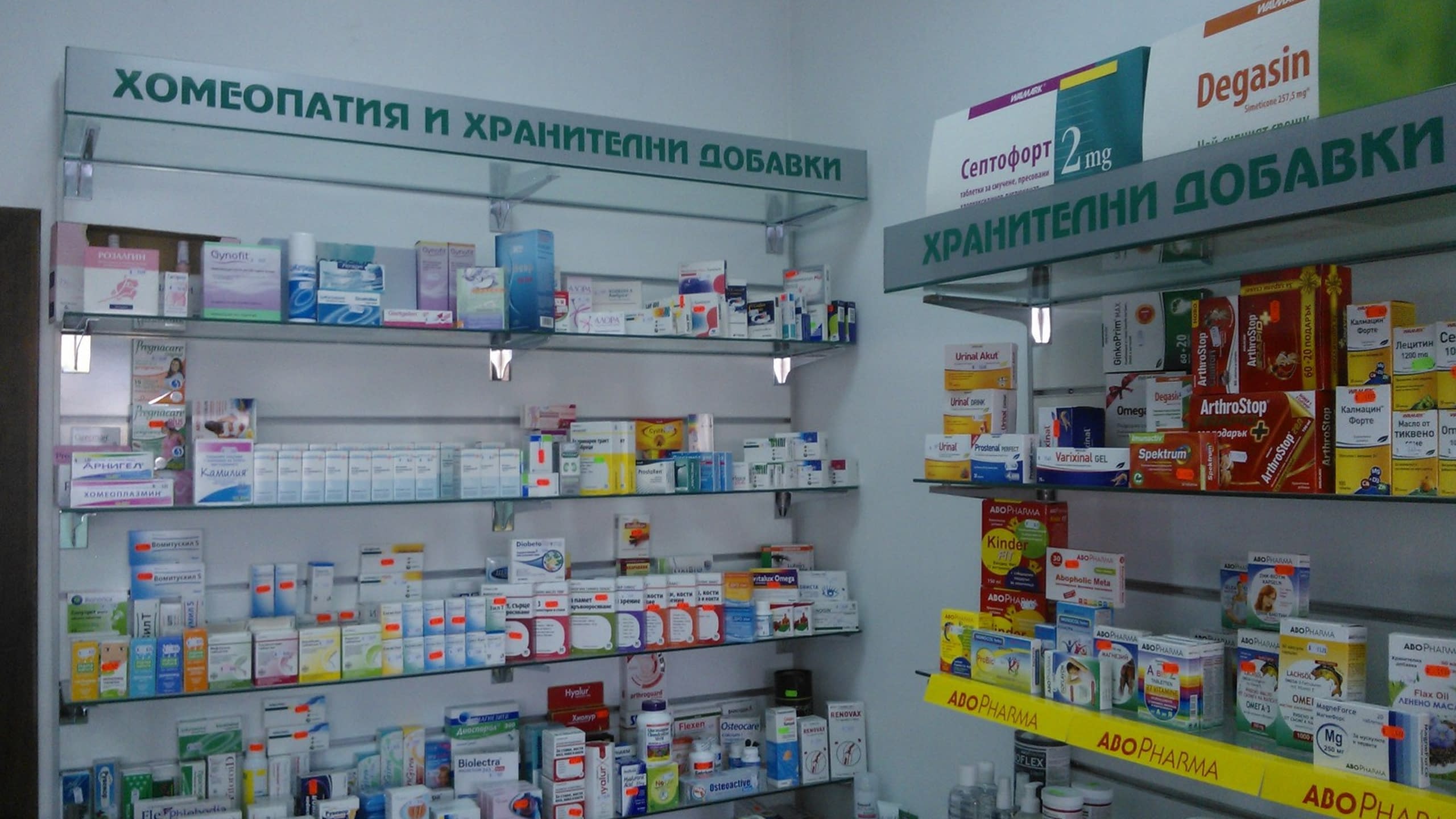 Рафтове в аптека с надписи от фолио, обозначаващи секторите "Хомеопатия" и "Хранителни добавки".