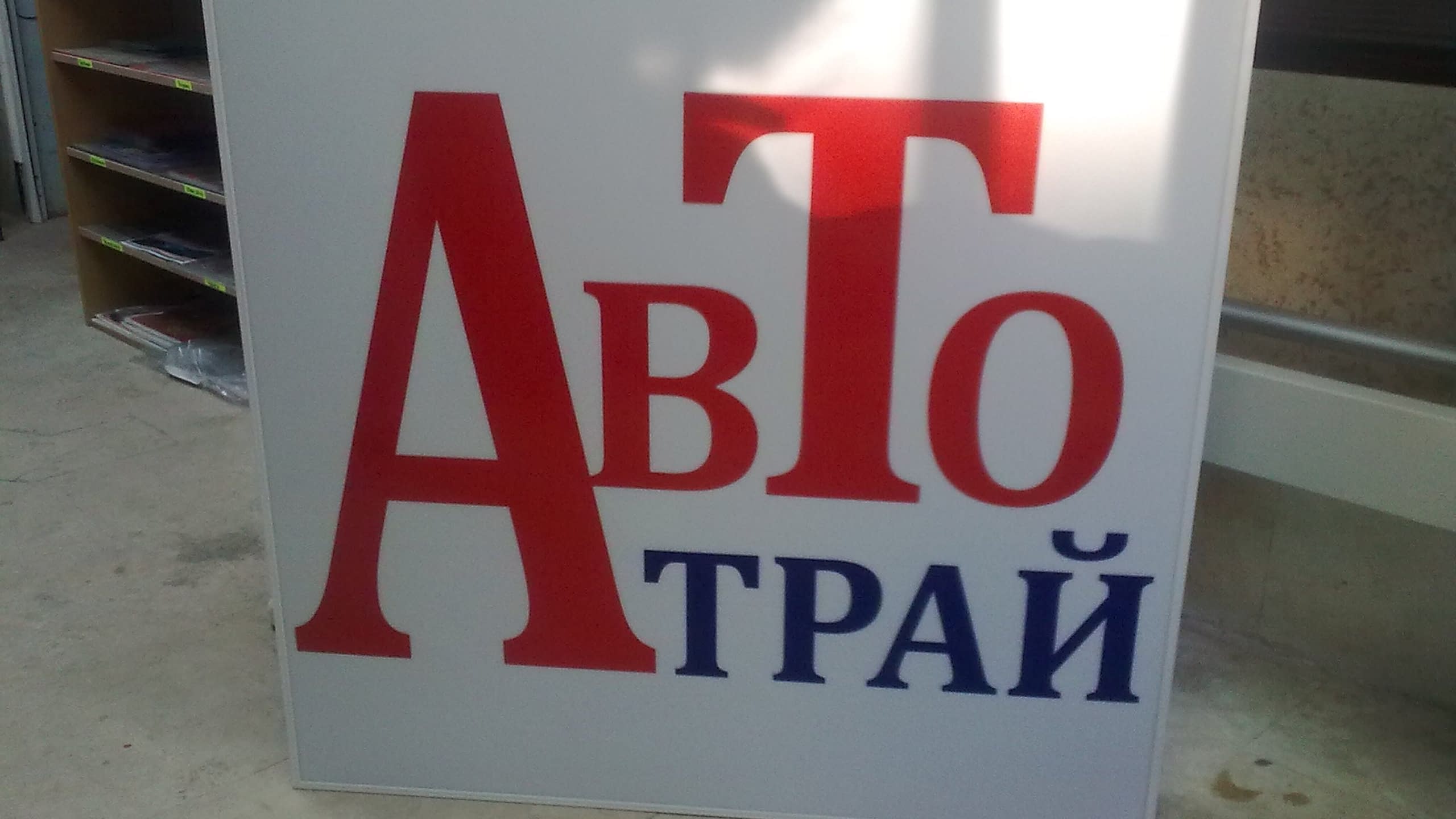 Правоъгълна табела с надпис "Авто Трай" с червени и сини букви на бял фон.