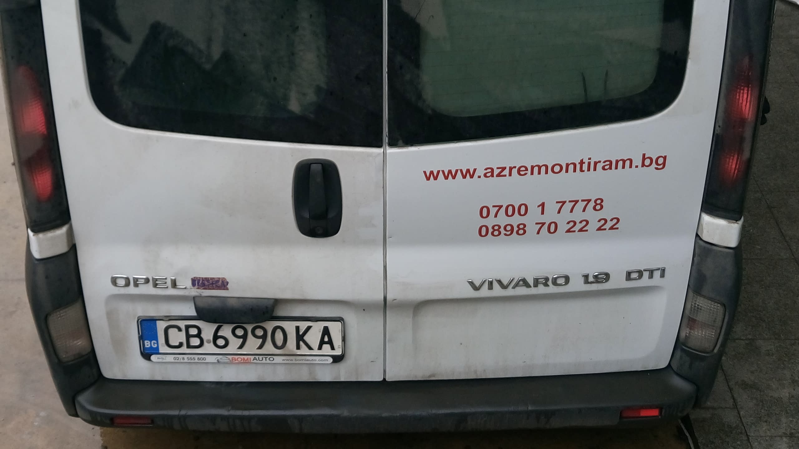 Задната част на бял бус Опел Виваро с изписани уебсайт и телефони за връзка.