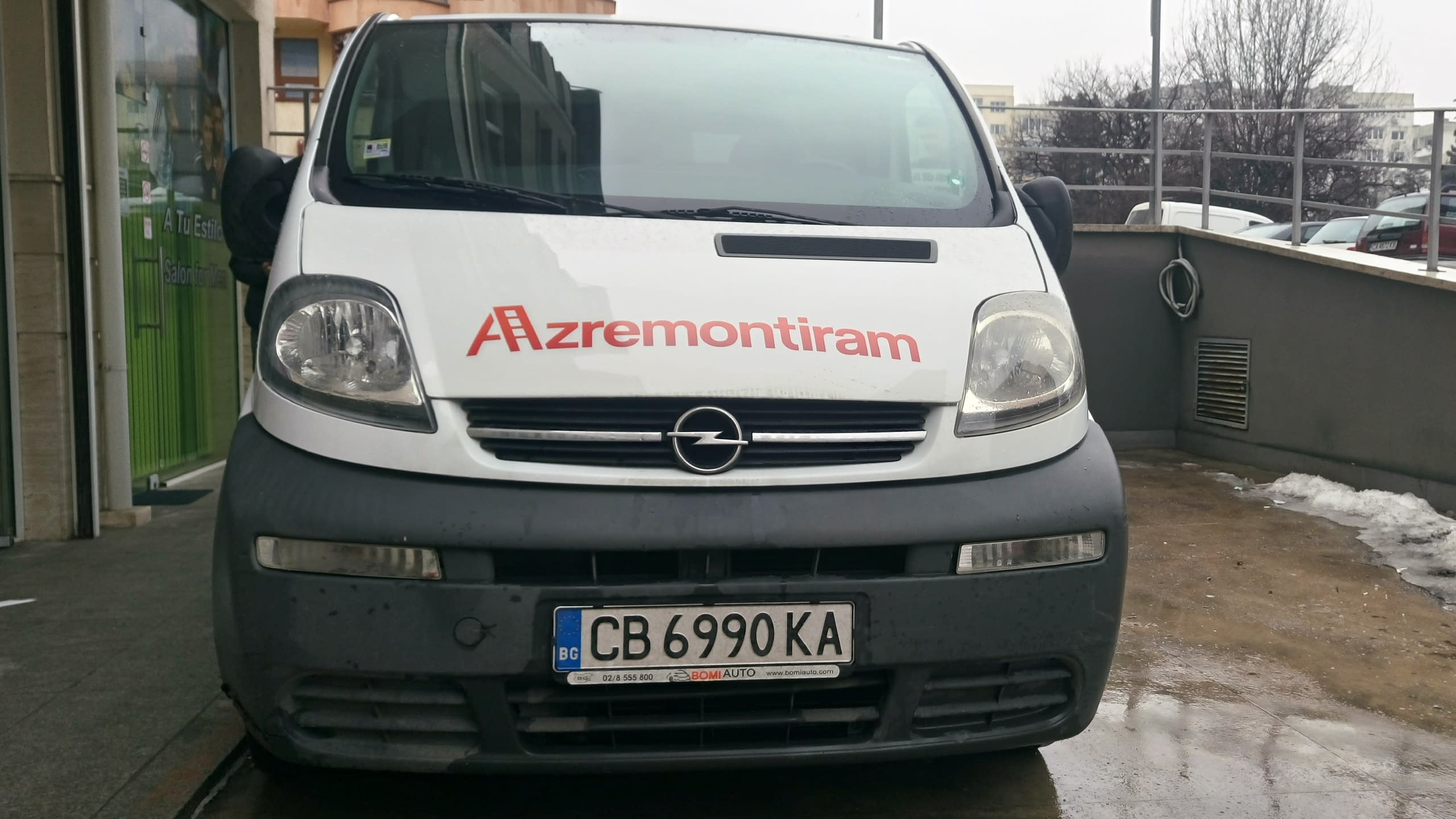 Челен изглед на бял бус Опел с червен надпис "Azremontiram" на предния капак.