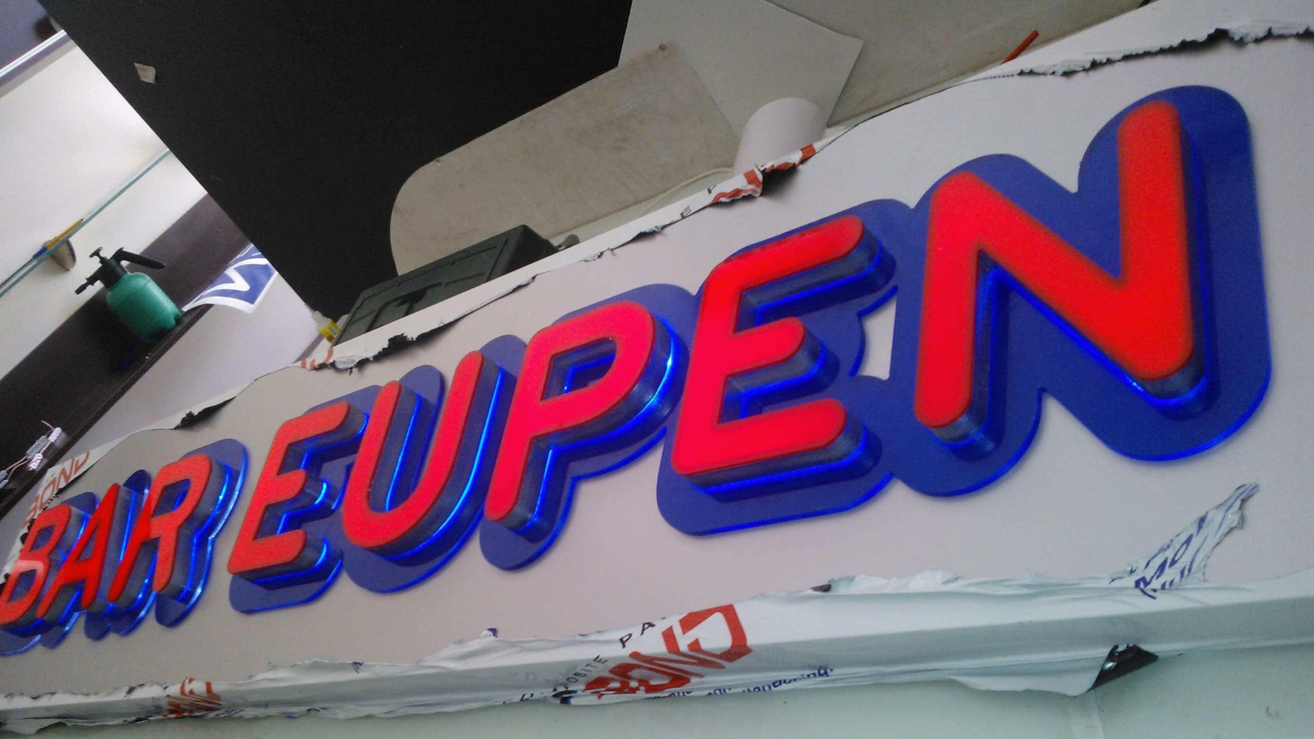 Близък план на светещи букви с червено и бяло осветление, обградени със син светещ контур.