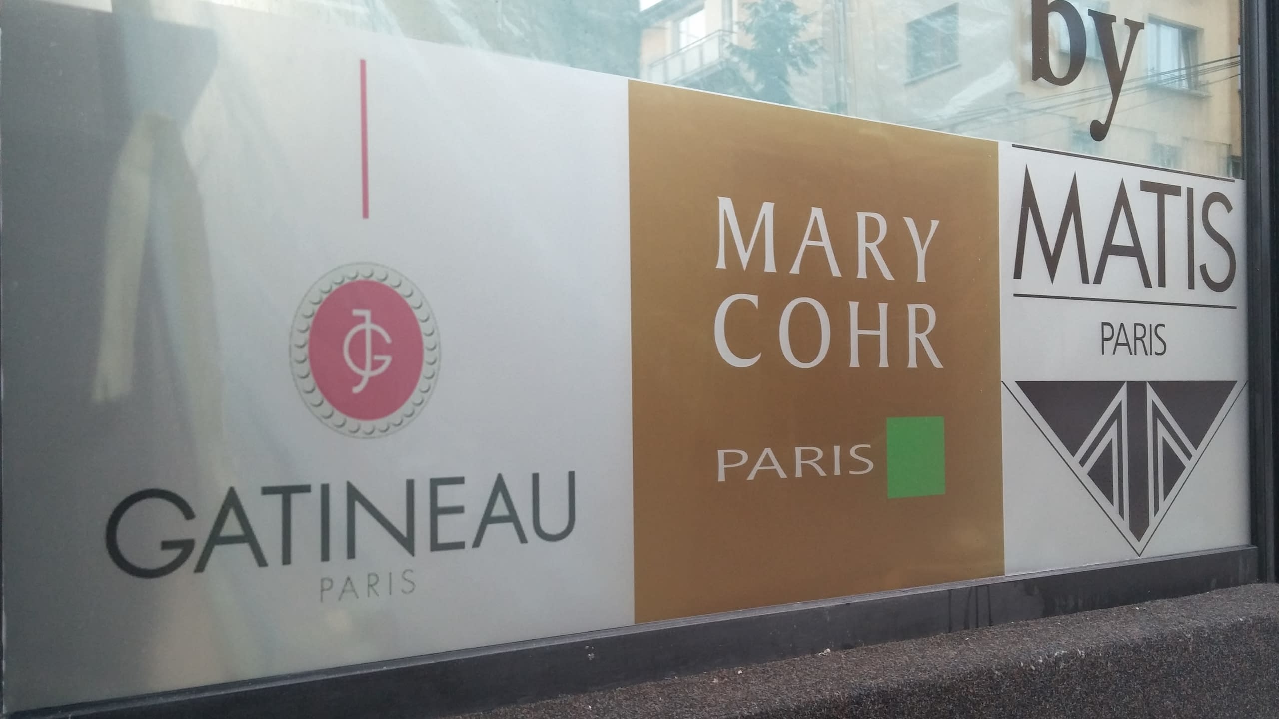 Част от облепена витрина, снимана под ъгъл, с логата на Gatineau, Mary Cohr и Matis.
