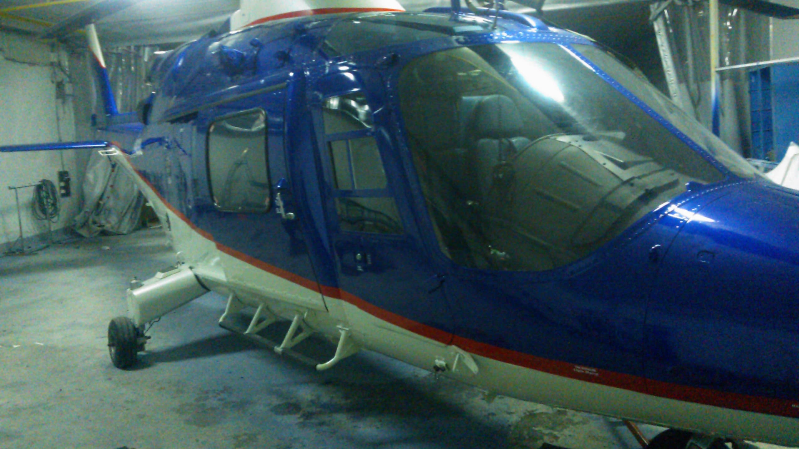 Близък план на пилотската кабина и вратата на син хеликоптер в хангар.