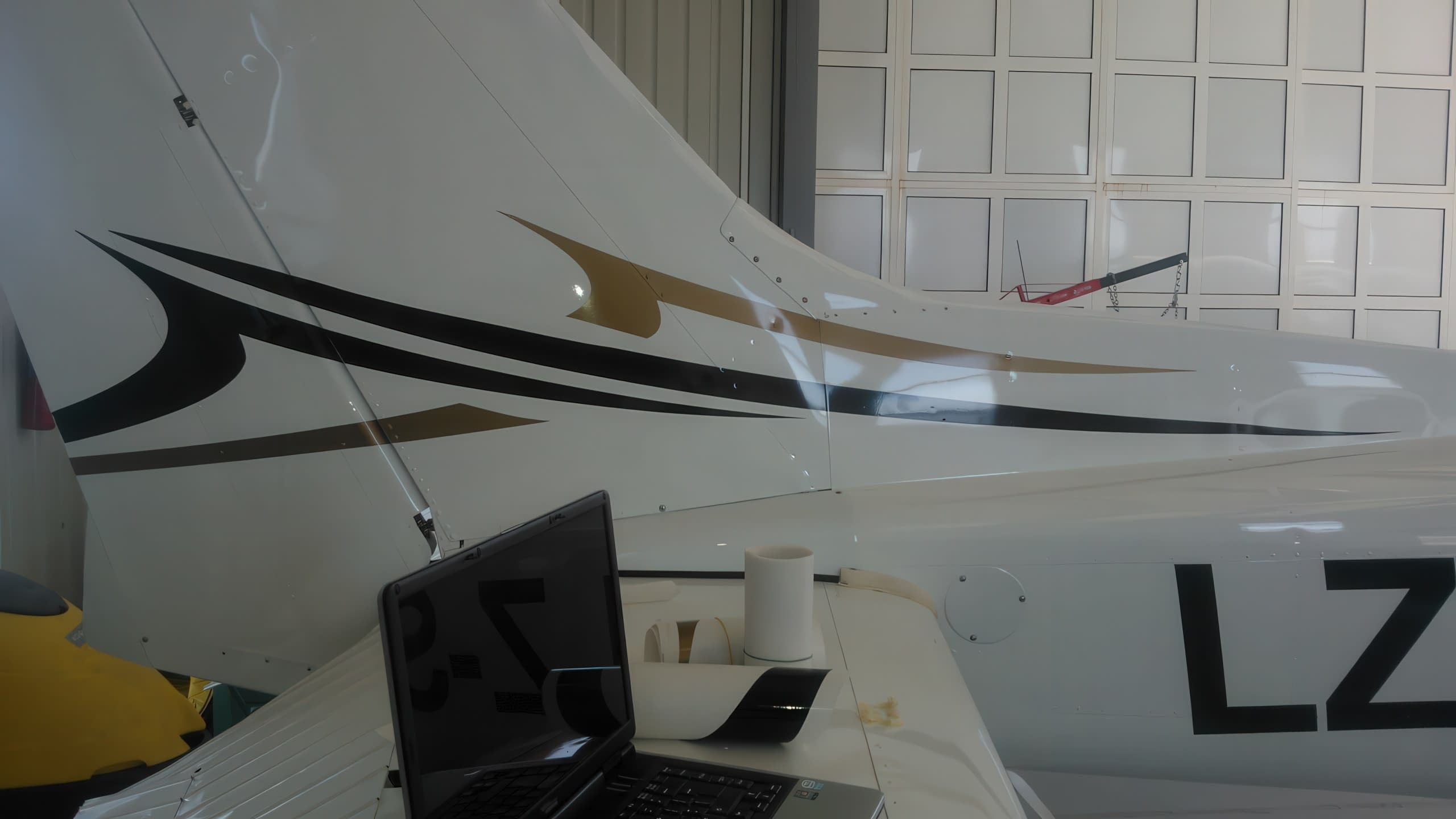 Процес по поставяне на стикери на опашката на самолет, с лаптоп и ролка фолио наблизо.