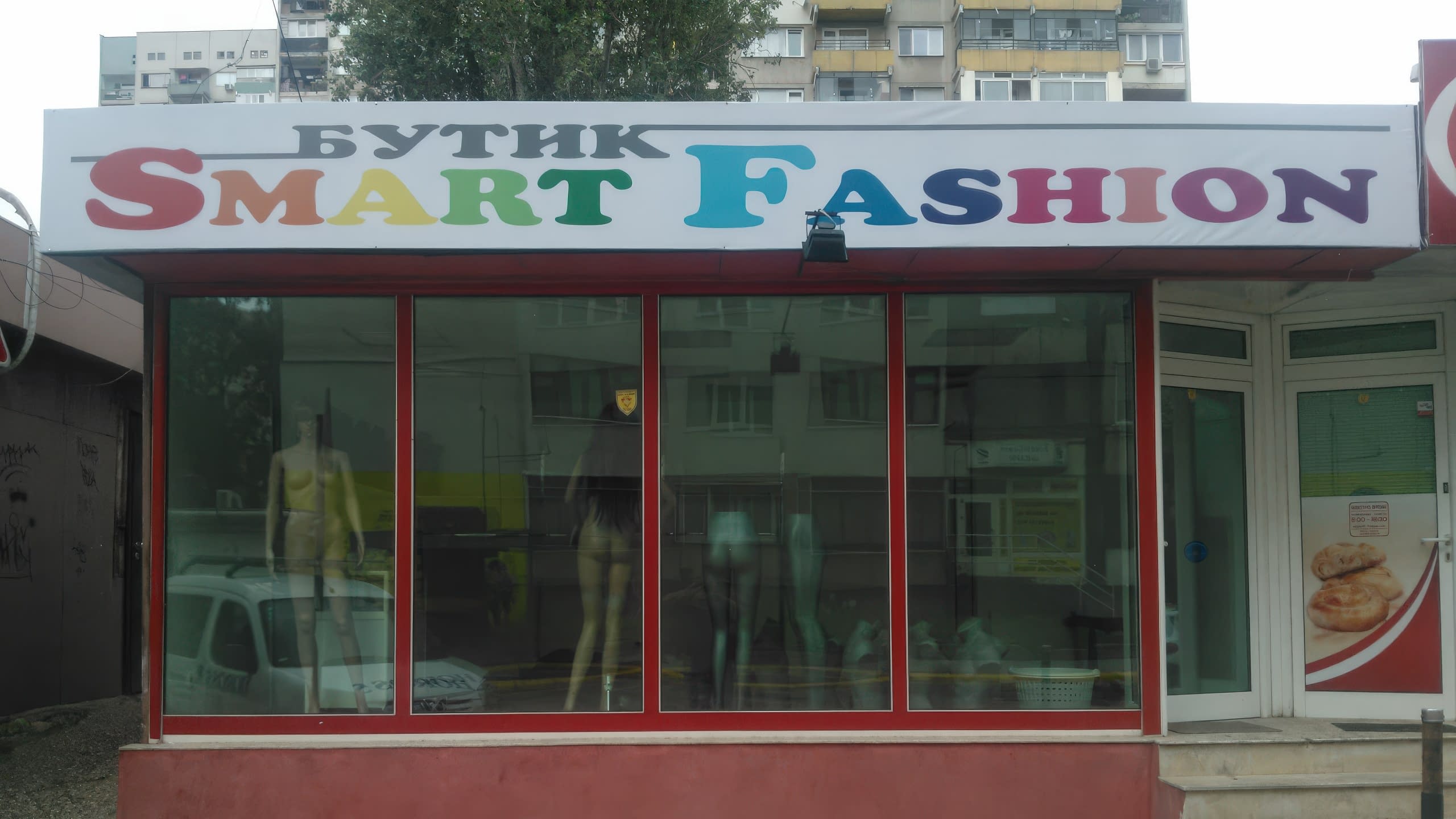 Табела на бутик "Smart Fashion" с разноцветни букви, монтирана над стъклени витрини с манекени.