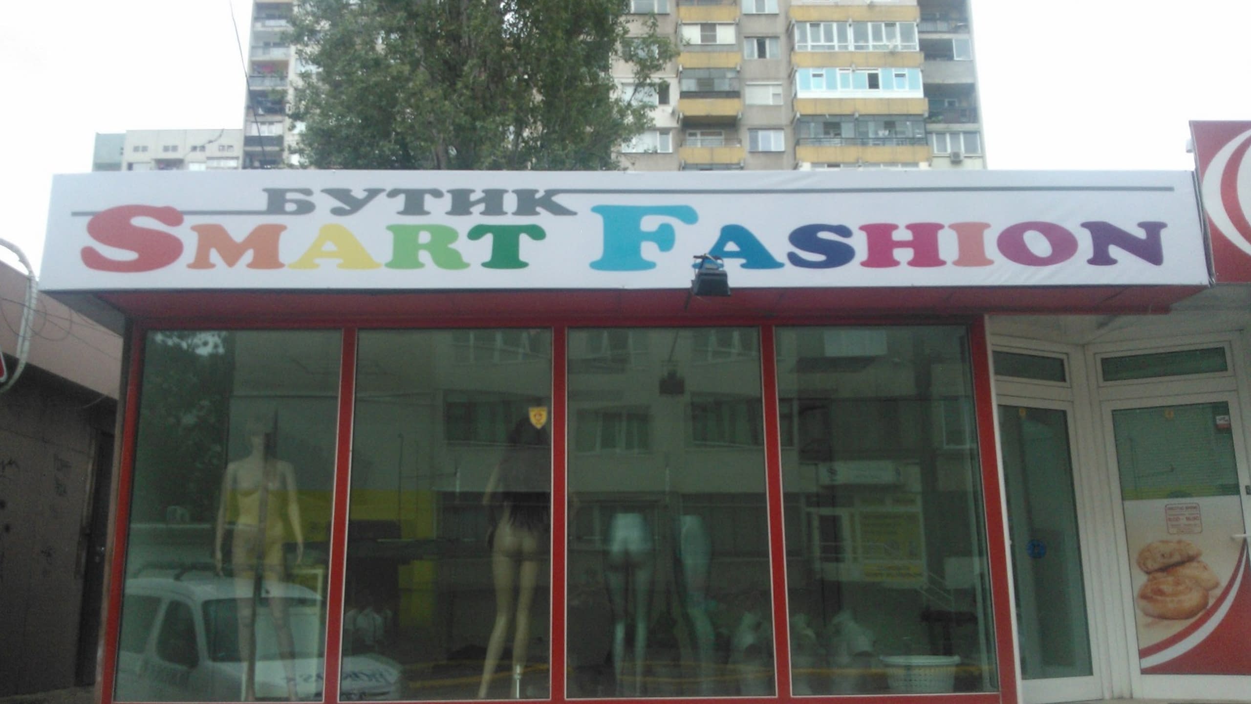 Голяма табела с цветен надпис "Smart Fashion" над витрината на магазин за дрехи.