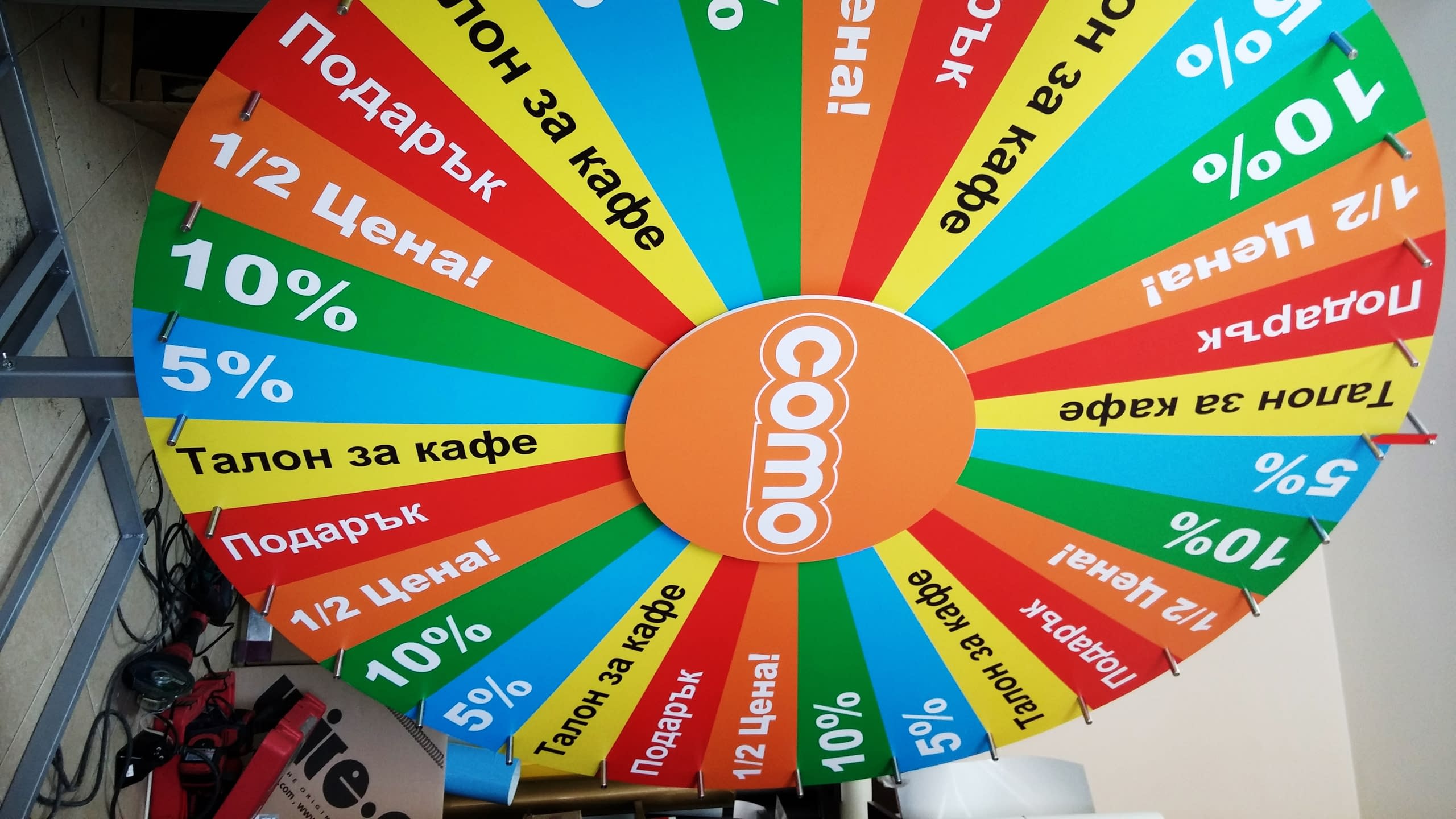 Близък план на разноцветно колело с надписи за отстъпки и подаръци и оранжево лого в центъра.