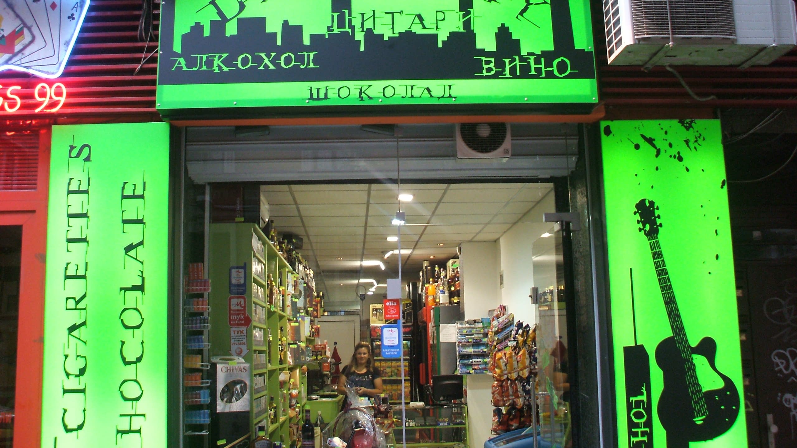 Вход на магазин „Dark City“, над който има светеща в зелено табела със силует на град и надписи.