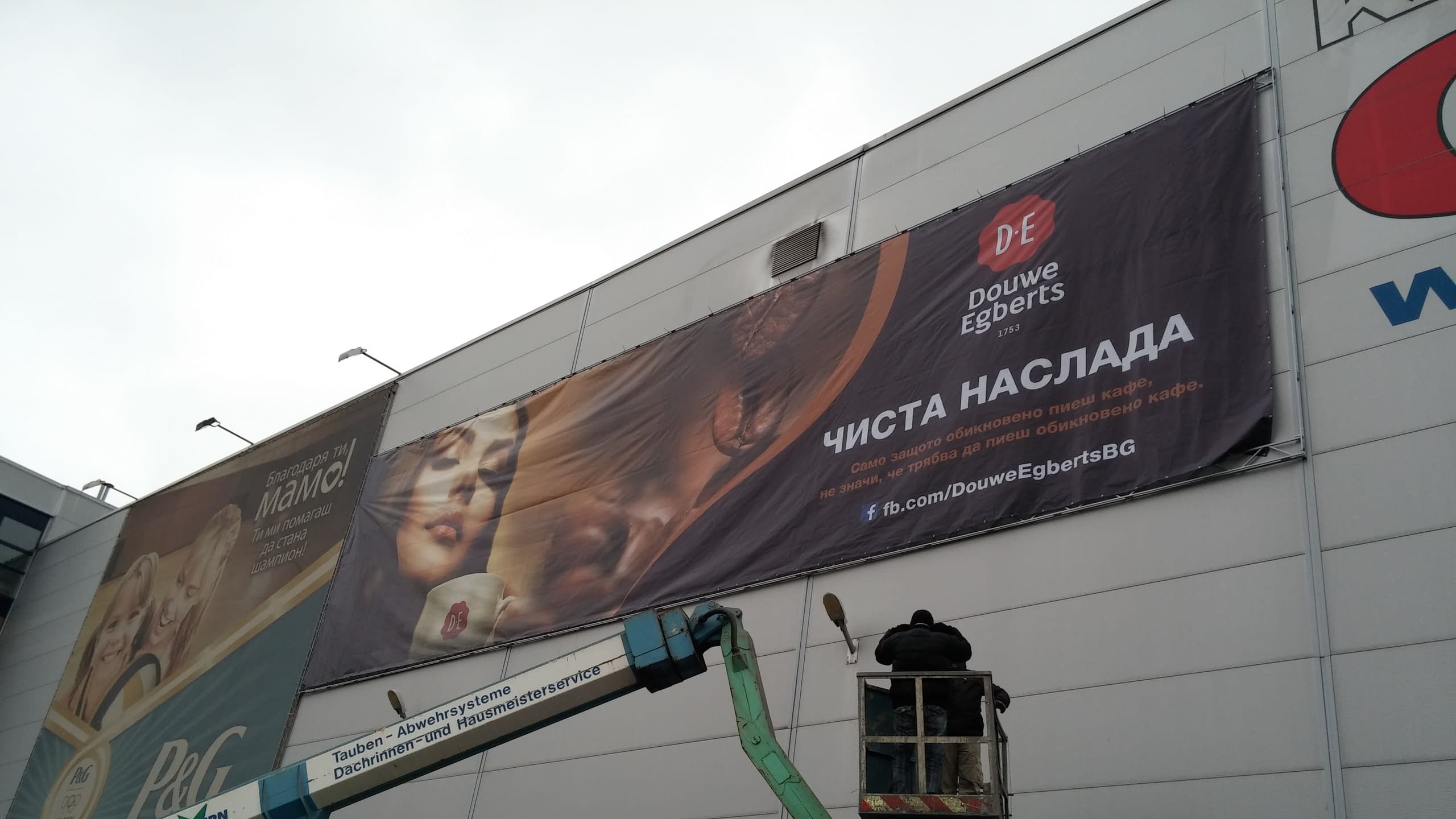 Близък план на монтаж на голям банер на стена на сграда, извършван от човек във вишка.