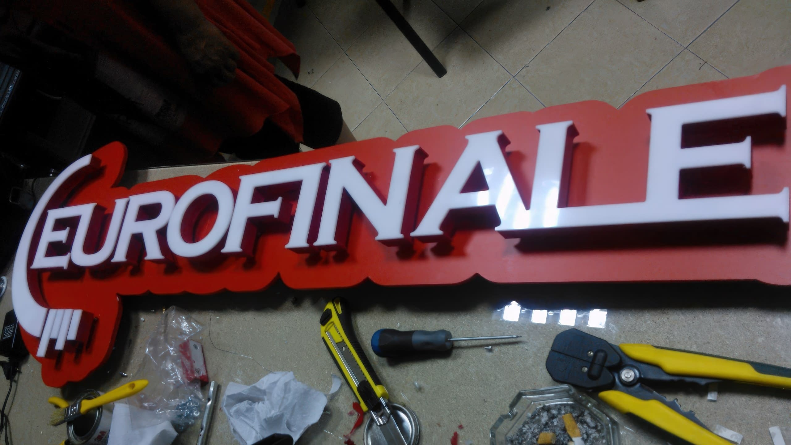 Близък план на табела с бели букви на червена основа, заобиколена от инструменти на работна маса.