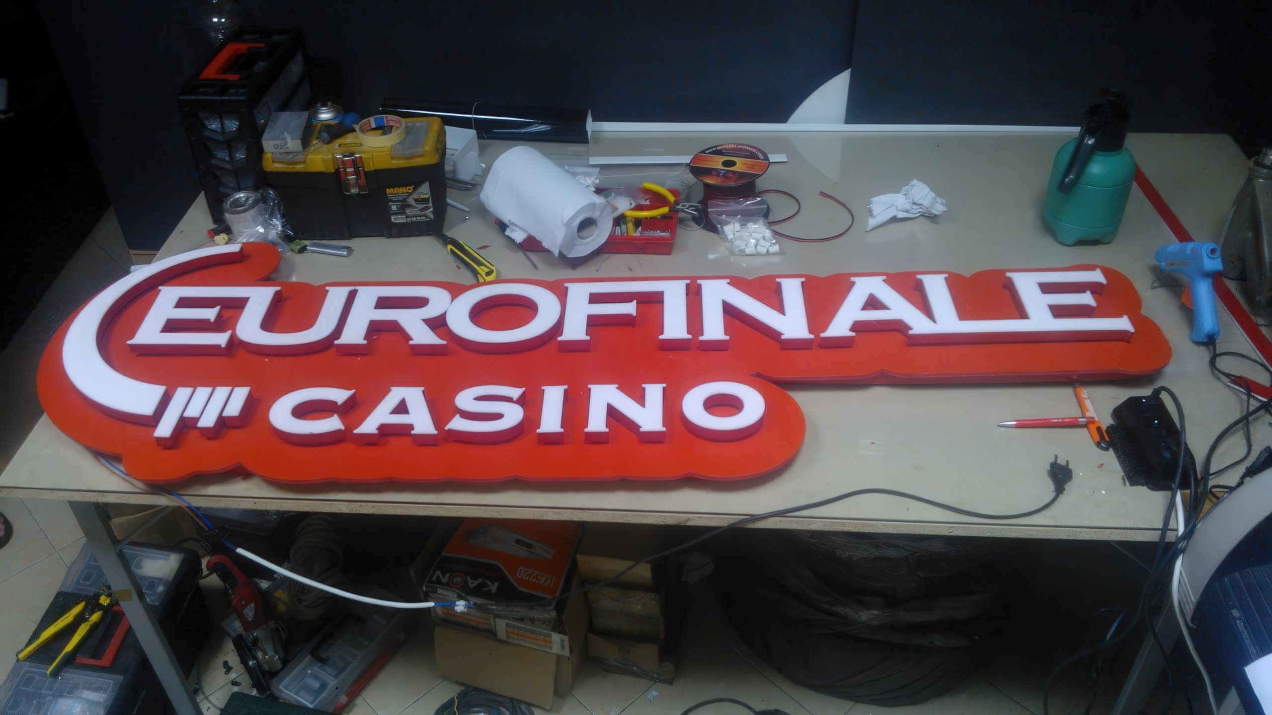 Цялостният вид на несветеща табела „EUROFINALE CASINO“ върху маса в производствен цех.