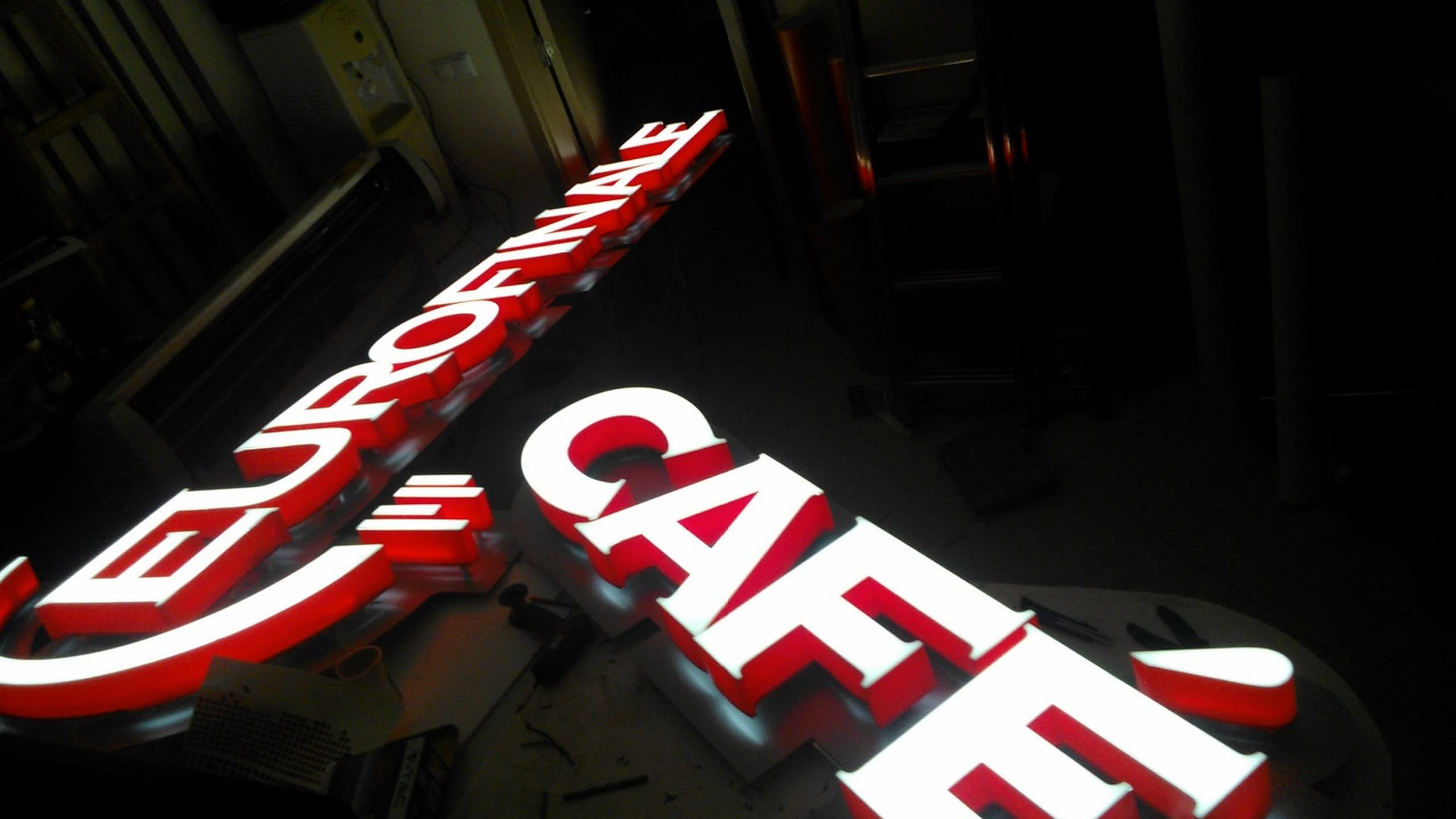 Два светещи надписа, „Eurofinale“ и „Café“, с бяла и червена светлина, заснети в тъмно помещение.