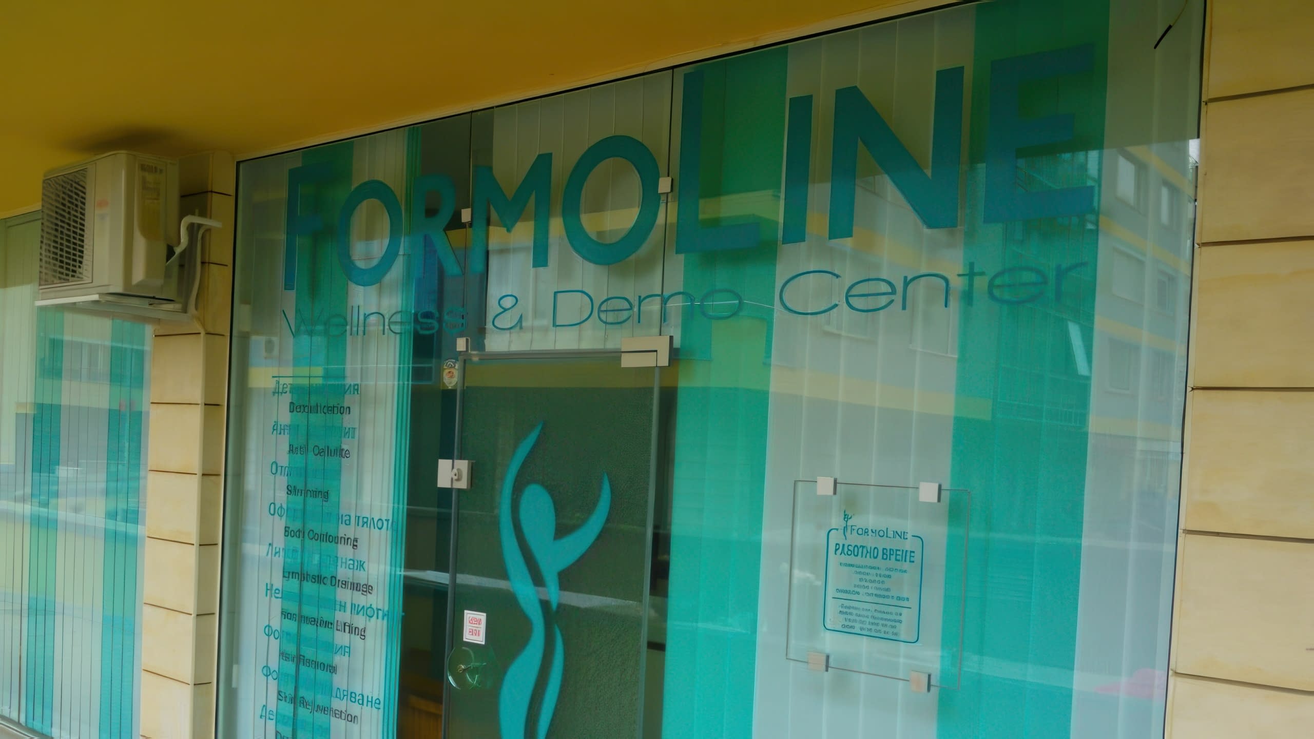 Стъклен вход на център Formoline, покрит с частично прозрачно фолио с графики и надписи.