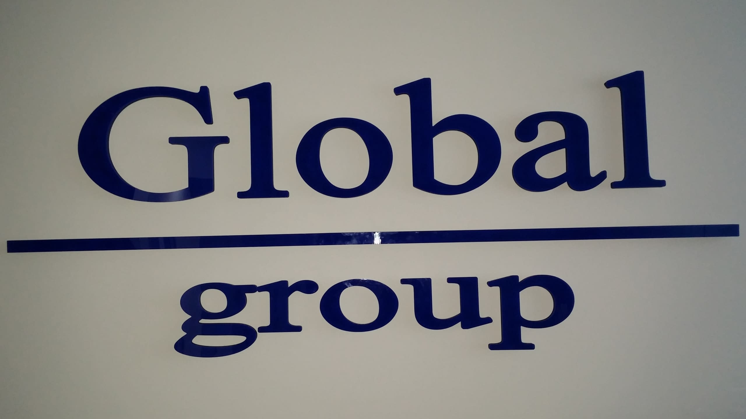 Тъмносини гланцирани букви, образуващи надписа „Global group“, монтирани на стена.