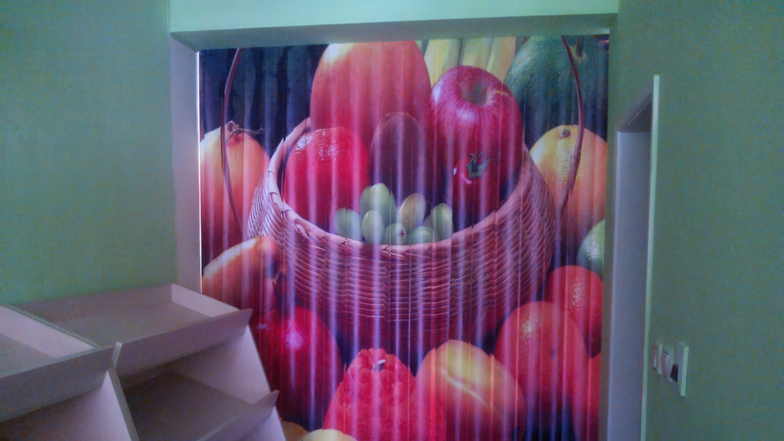 Цветен панален принт на плодове в кошница, монтиран в ниша на стена в търговско помещение с празни стелажи вляво.