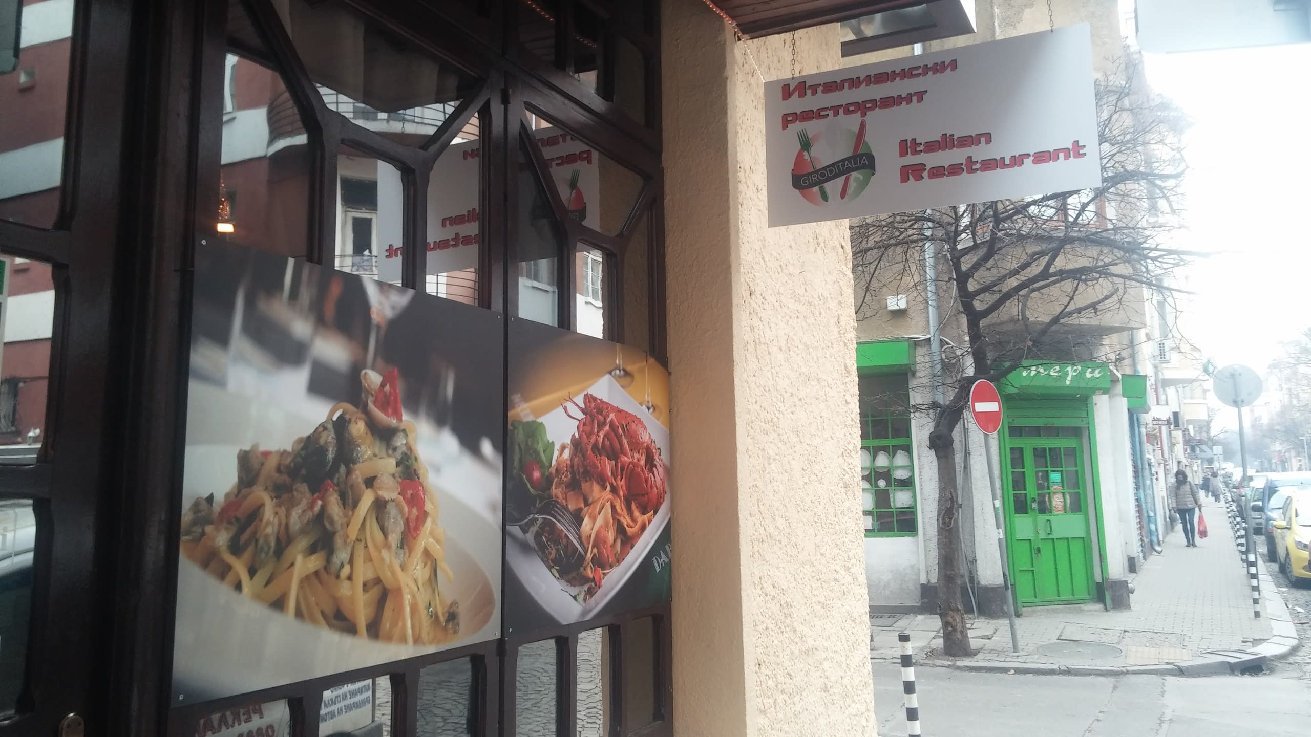 Вход на италиански ресторант с табела и рекламни снимки на паста на витрините.