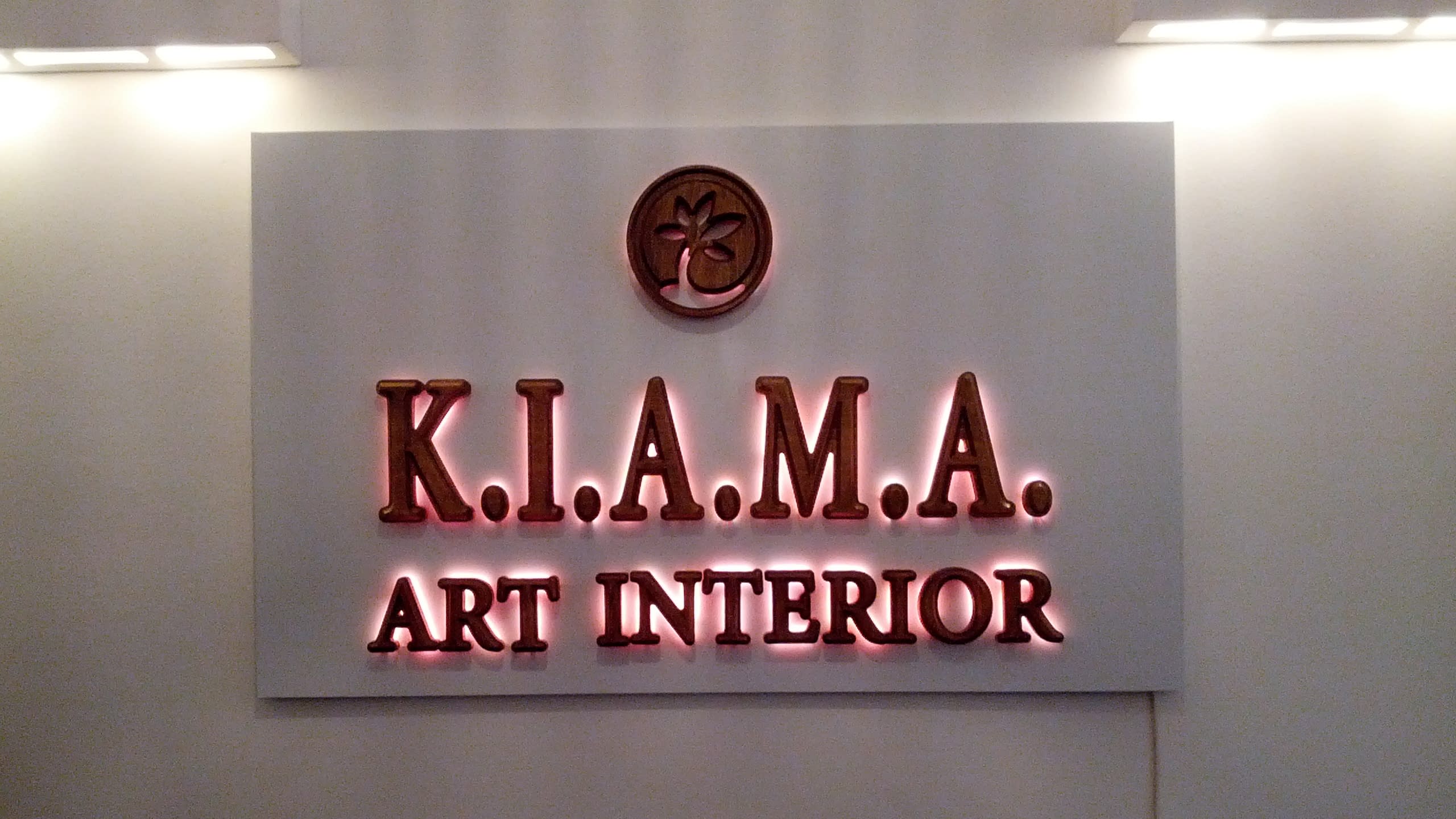 Светеща табела с букви с дървесен ефект, монтирана на стена и осветена отгоре с лампи.