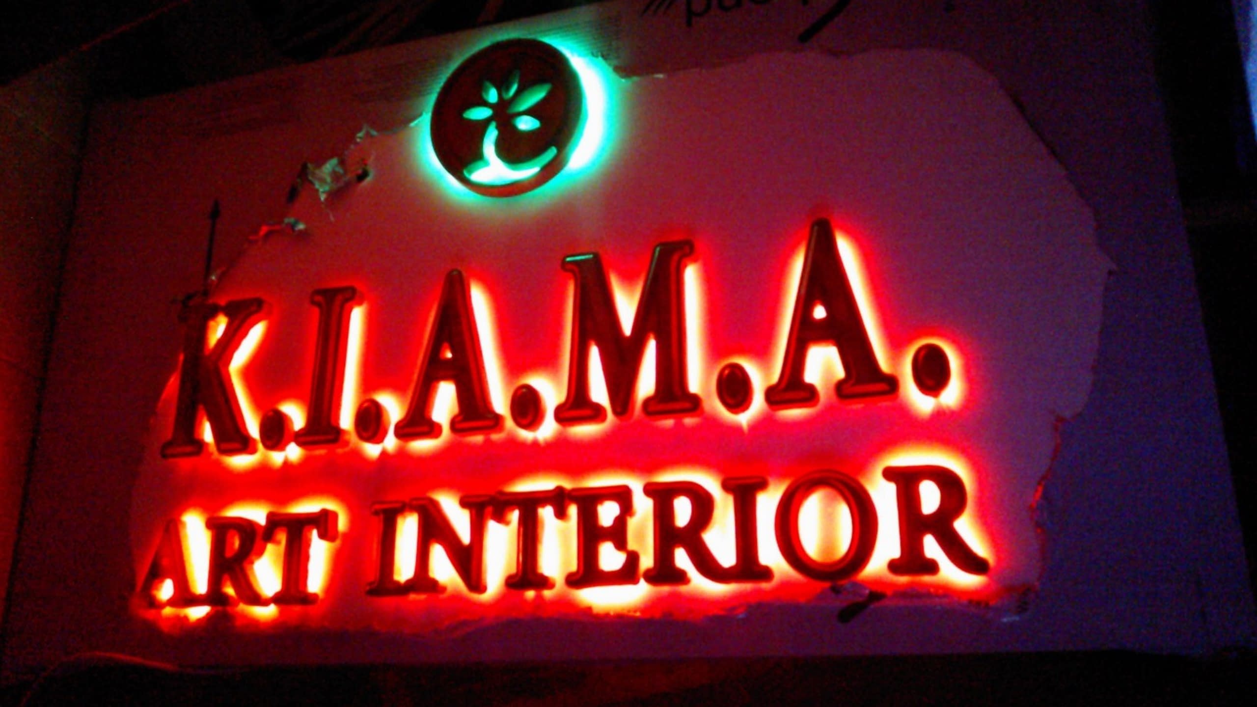 Обемни букви с името на фирмата и нейното лого, осветени отзад с наситена оранжево-червена светлина по време на изработка.