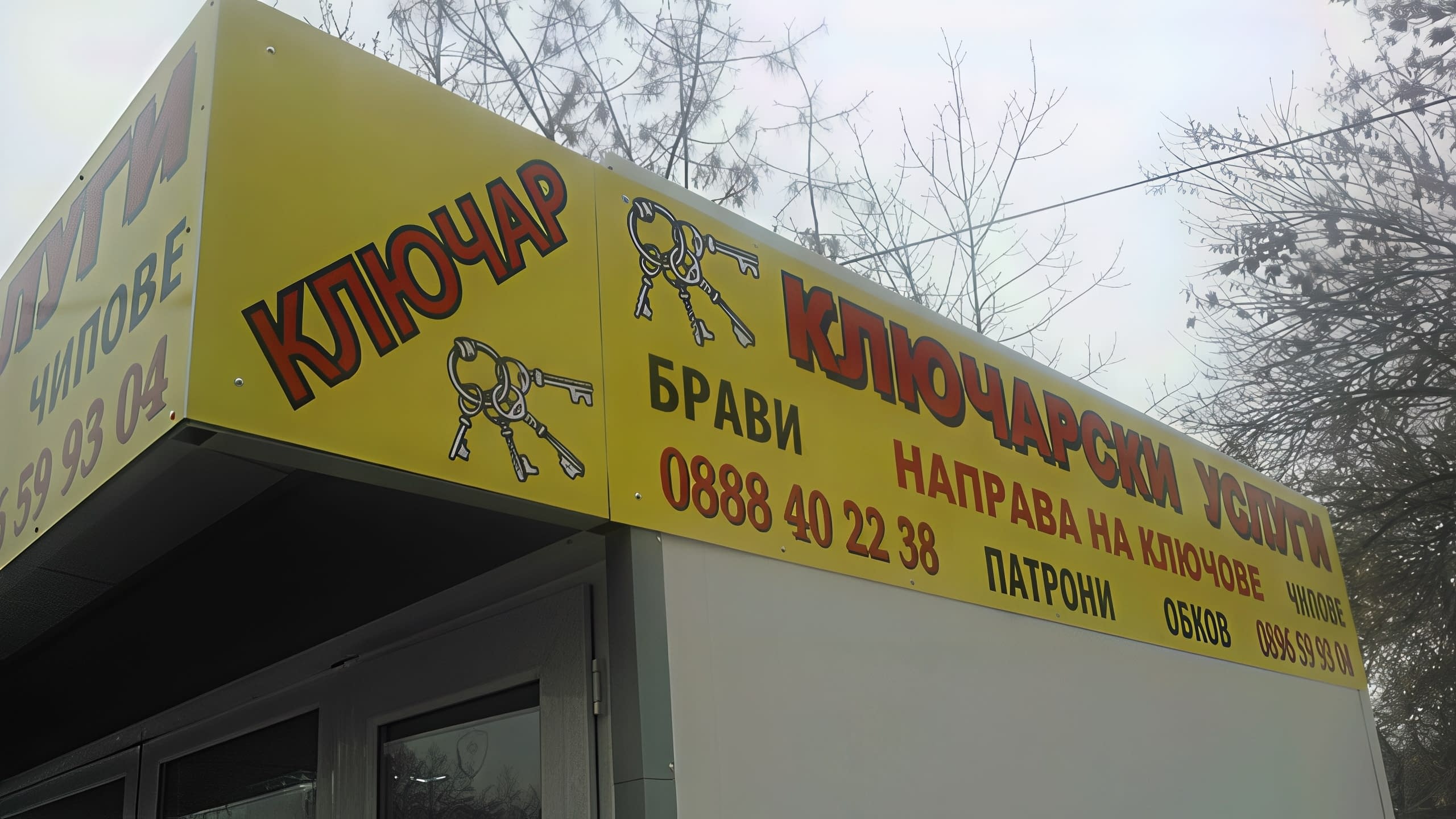 Близък план на ъгъла на жълта информационна табела за ключар, изброяваща услуги и телефонни номера.
