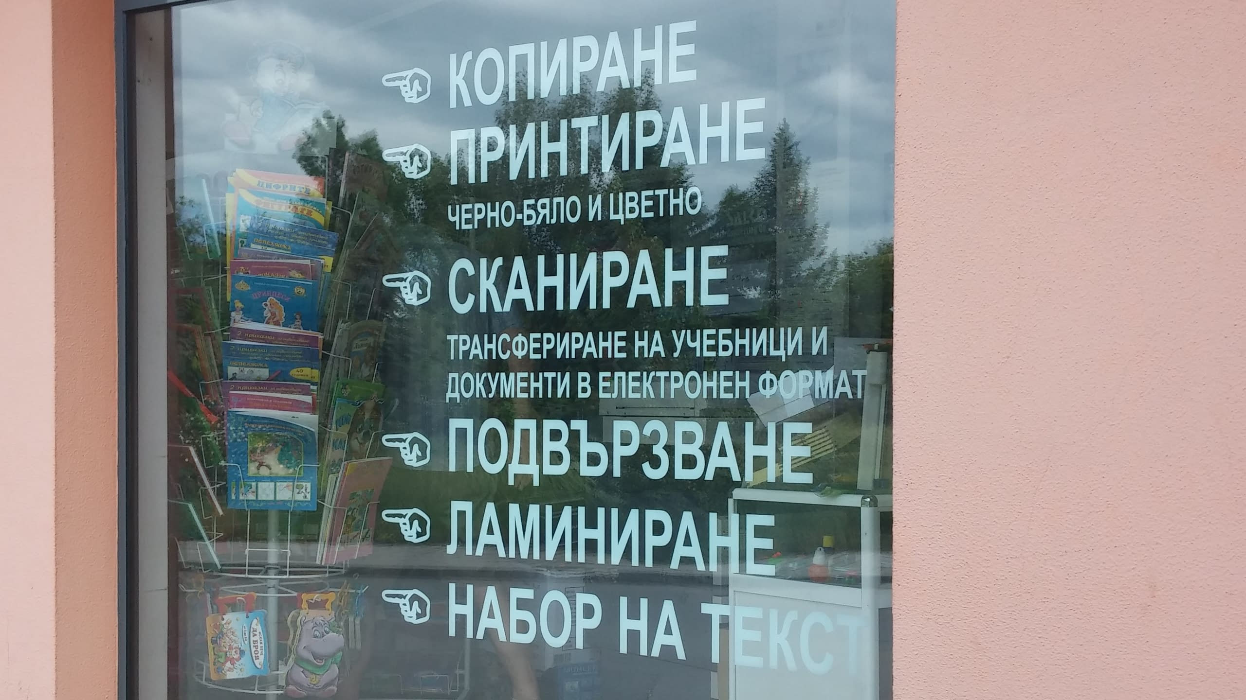 Близък план на надпис от бяло фолио на витрина, изброяващ услугите на копирен център.