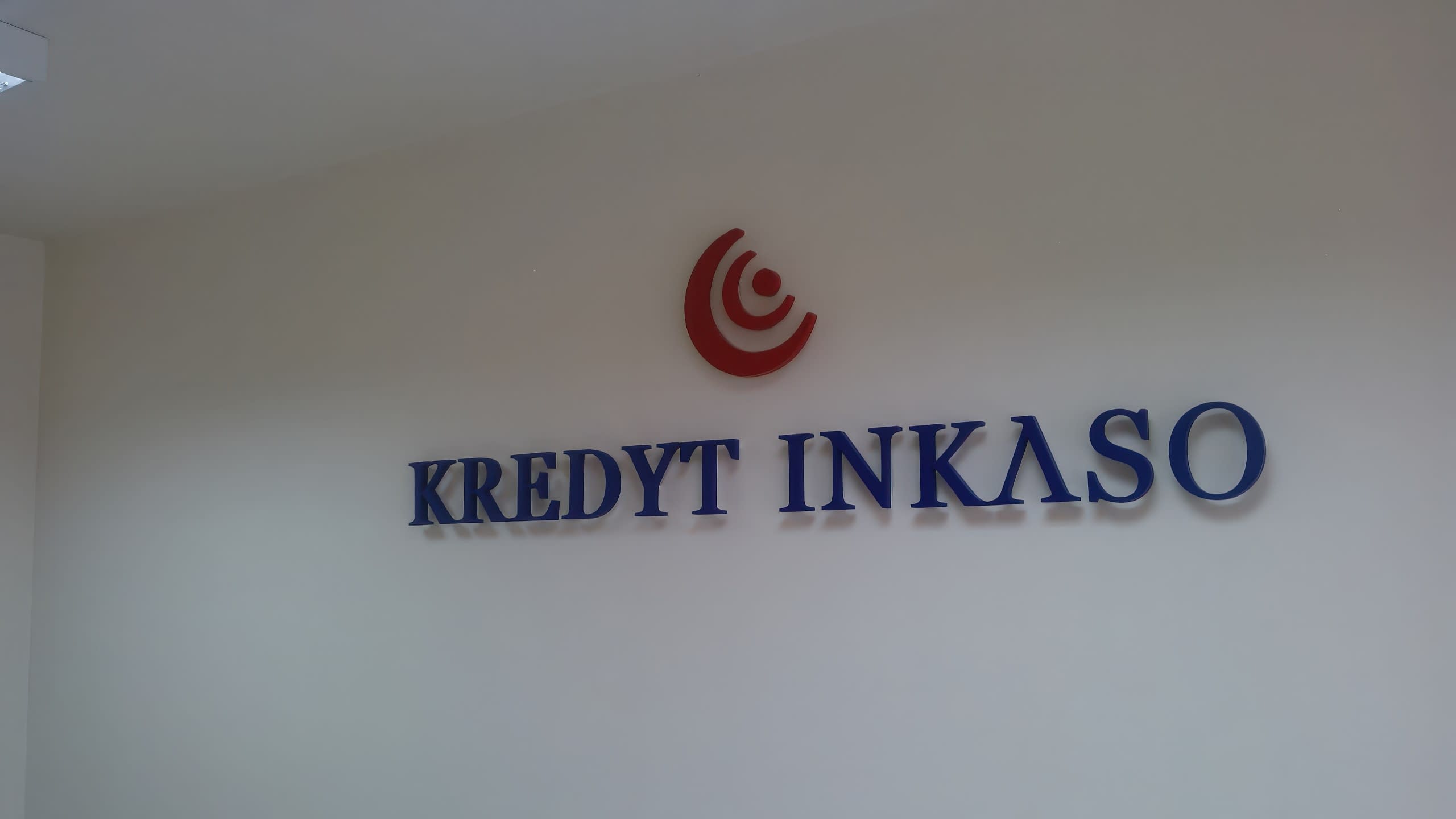 Фирменото лого на KREDYT INKASO, монтирано на светла офис стена и заснето от разстояние.