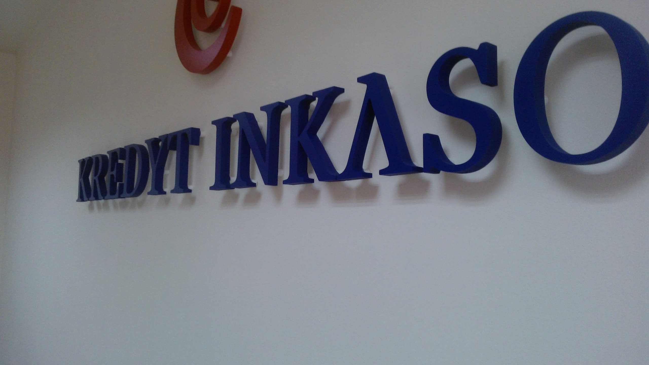 Сини обемни букви на надпис KREDYT INKASO, заснети отстрани под ъгъл, за да се види тяхната дебелина.