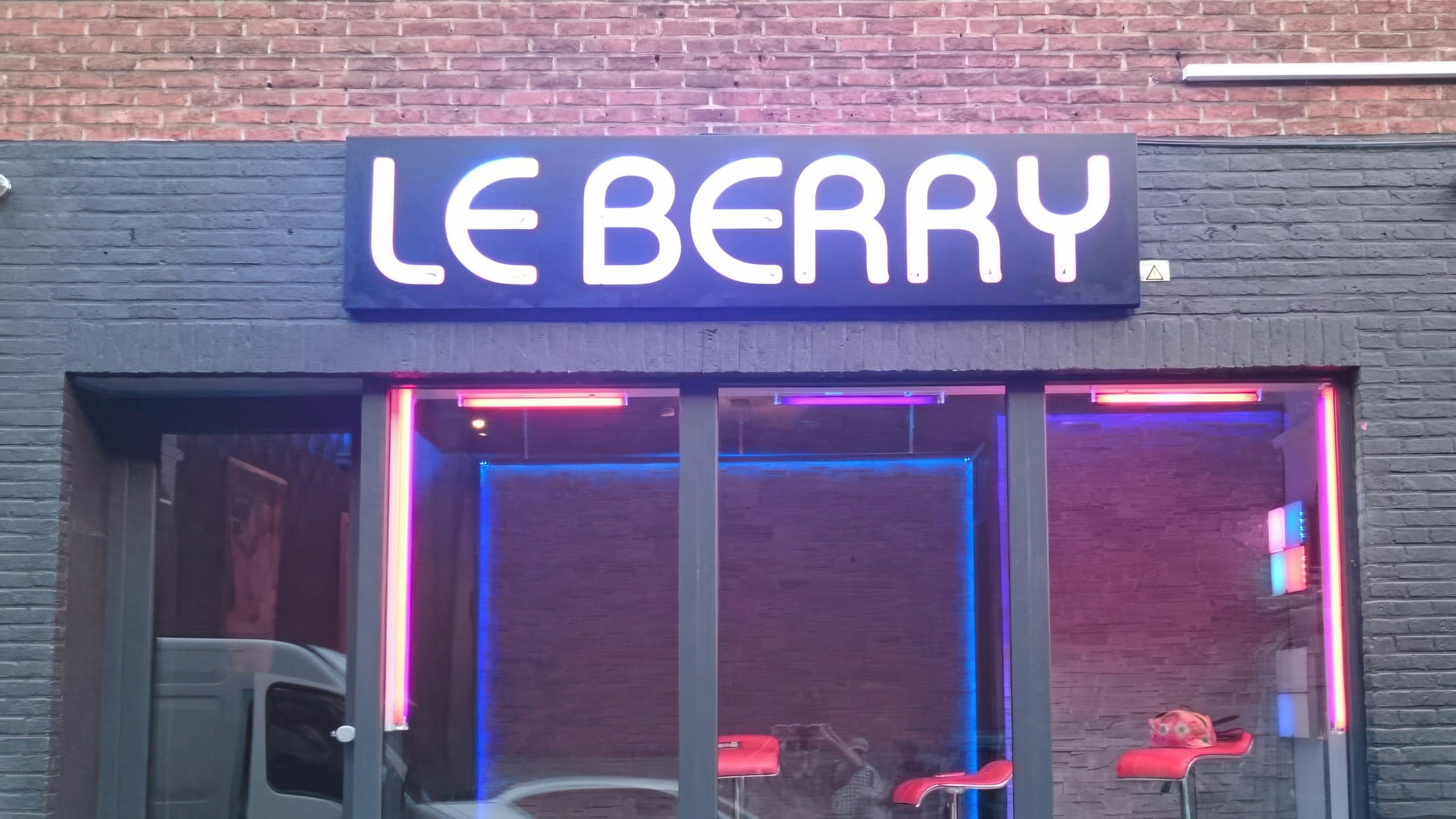 Изглед към фасадата на заведение с голям светещ надпис LE BERRY и витрини с червени бар столове.